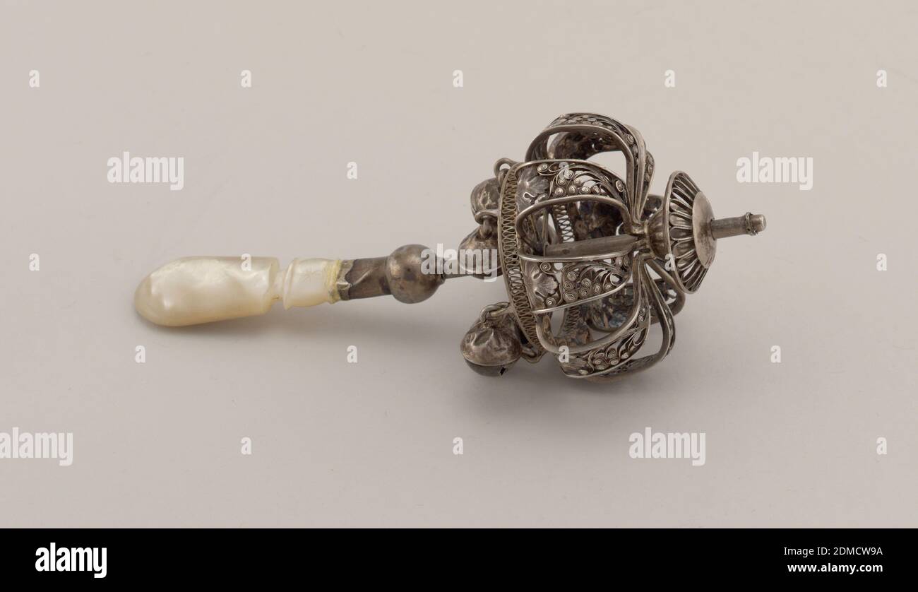 Rattle, Silver, mother-of-pearl, Open cage formed of eight silver filigree straps featuring delicate scroll and leaf motifs on each, straps attached to ball above, which rotates and slides up and down central post; attached to base of cage is circular, filigree frame, beneath which hang 6 bells on links (five bells are unadorned; a sixth, which is evidently a replacement, features leaf motifs); 6 structural spokes extend inward from links to ring attached to central post; small domed disc with filigree work situated above cage, which also rotates and slides up and down post; stationary ball Stock Photo