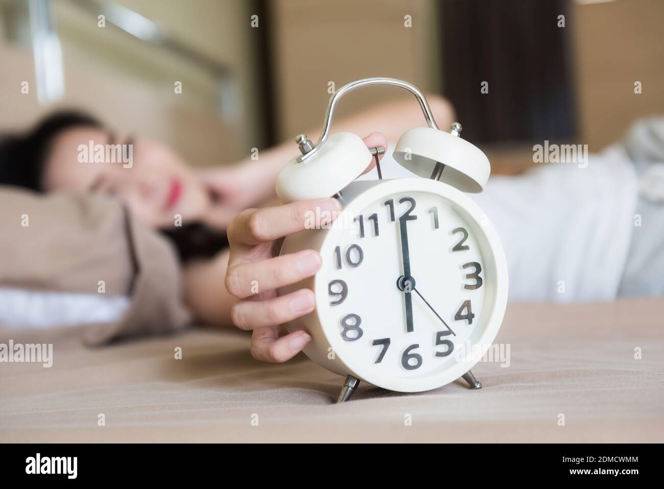 Asian beautiful woman wake up on bed to turn off white alarm clock at 6 am  in her bedroom. Set up alarm to get up to go working in weekday Stock Photo  -