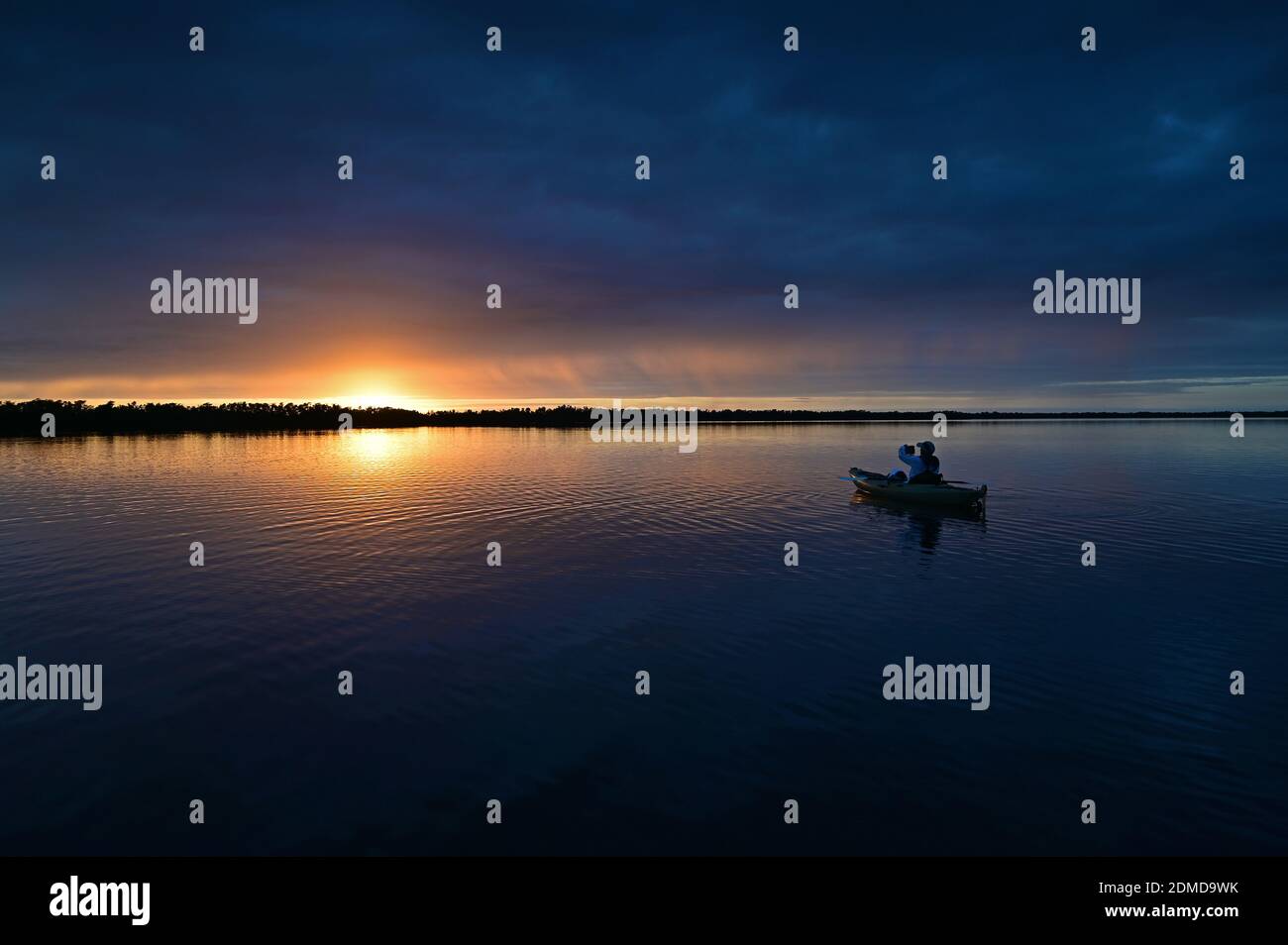 Distant kayaker at sunset on Coot Bay in Everglades National Park, Florida under winter cloudscape reflected in tranquil water. Stock Photo