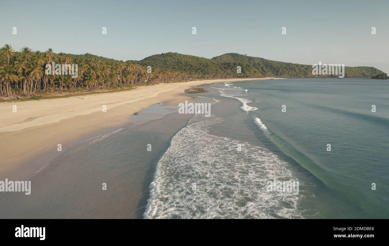 Waves drop to sand sea shore aerial. Wavy seascape of ocean bay. Sandy coast with tropic forest. Hills with green jungles of palm trees. Paradise vacation on El Nido Island, Philippine, Asia at summer Stock Photo