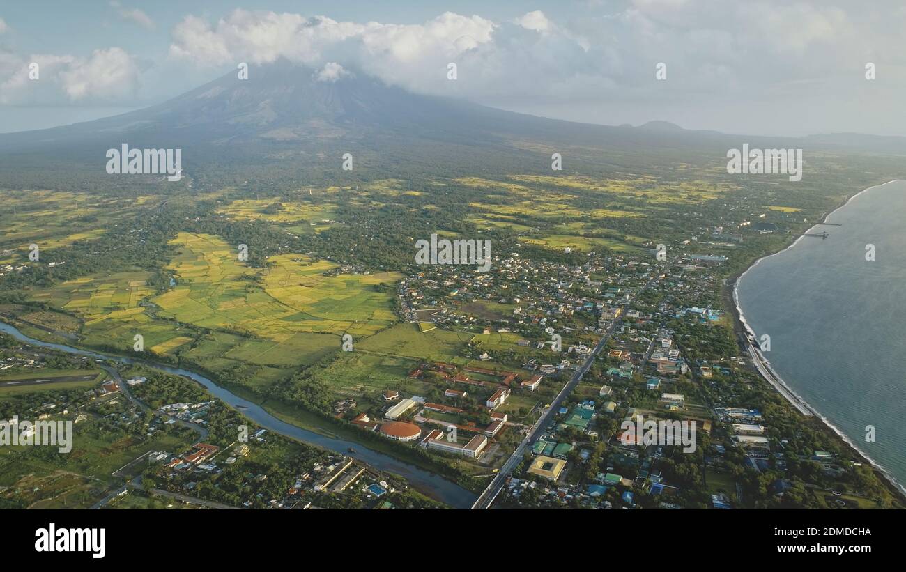 Tropic cityscape at sea bay river banks aerial. Streets with cottages and lodges with traffic road. Green valley at Mayon volcano Legazpi city, Philippines. Nobody nature landscape at mist haze Stock Photo