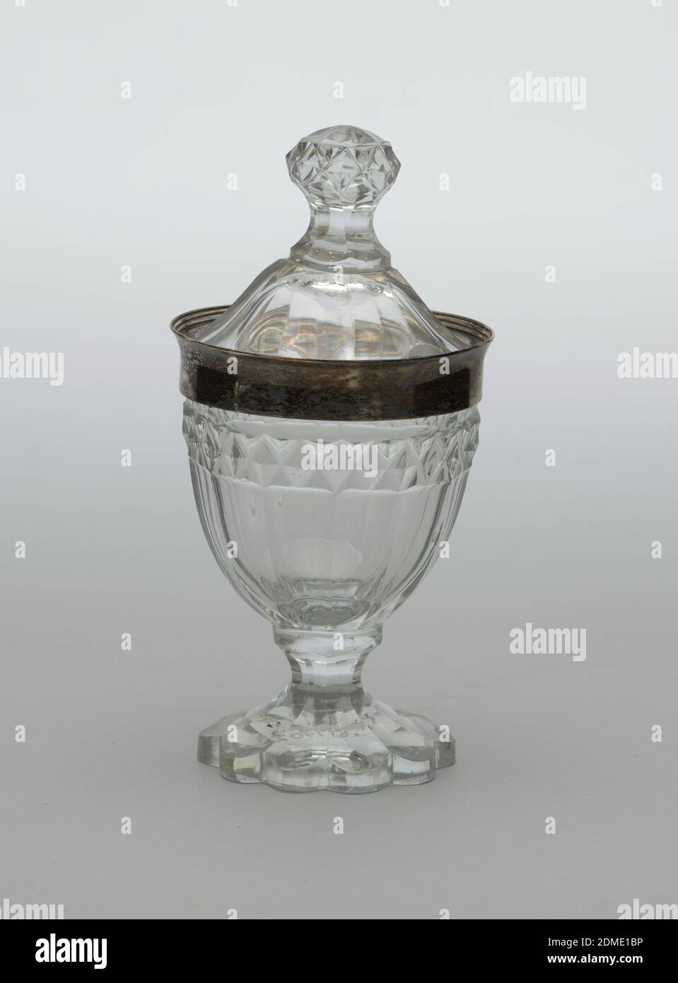 Jar and cover, Henry Chawner, 1764 – 1851, glass, silver, Flattened urn-shaped body on tall faceted flaring foot with scalloped edge;sides of body fluted, a band of diamonds above, above that a band of silverwith slightly everted lip; high domed cover with faceted sides and finial cut with diamonds, notch cut out of rim for spoon., London, England, ca. 1795, glasswares, Decorative Arts, Jar and cover Stock Photo
