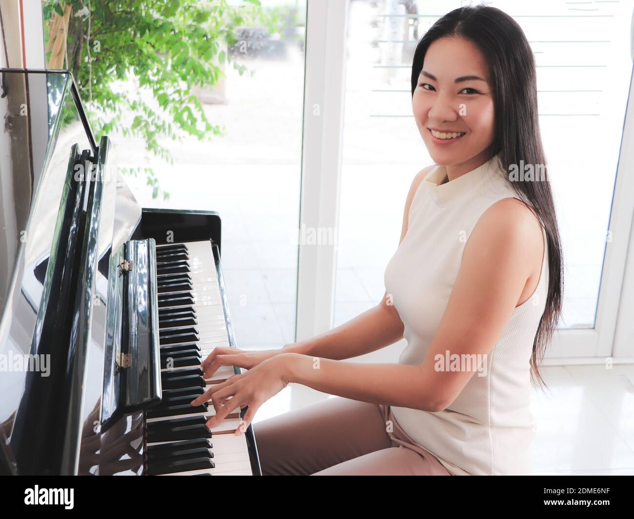 Asian young woman playing piano upright in the white room and smiling at  the camera Stock Photo - Alamy
