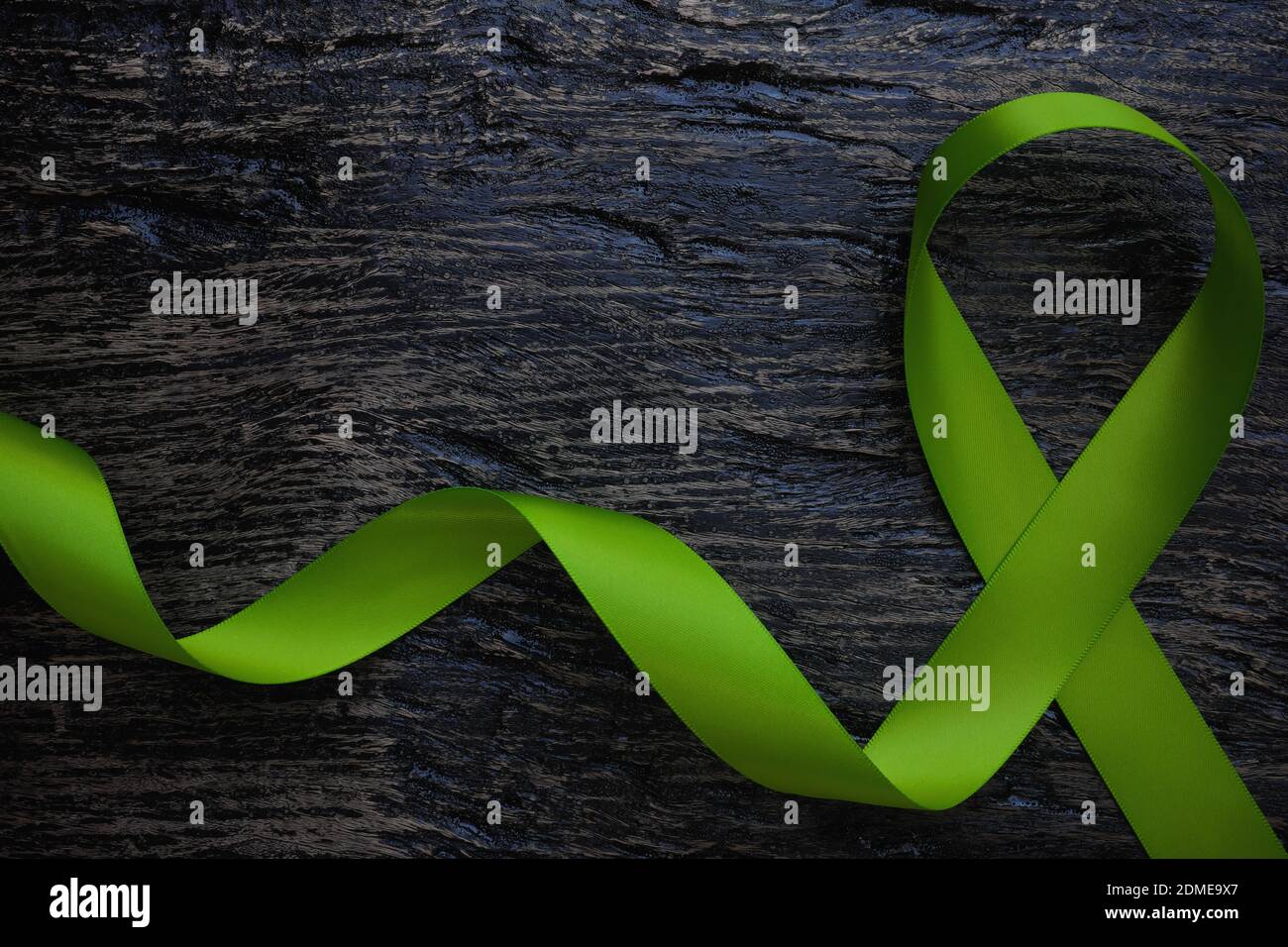 Top view of lime green color ribbon on dark background. Non-hodgkin lymphoma cancer, lyme disease, muscular dystrophy and postpartum depression Stock Photo