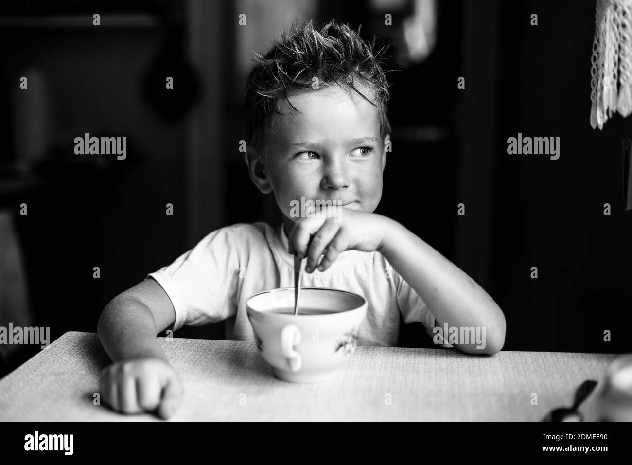 Funny little boy is drinking tea at the table in home. Black and white ...