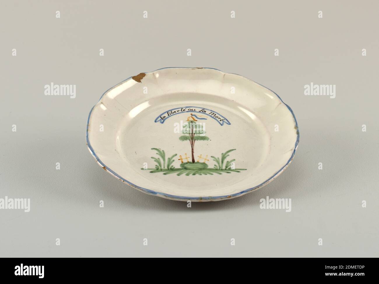 Plate, Tin-glazed earthenware, Steep curved marly, eight-sided scalloped edge with blue band. In center, a tree crowned by cap and banner, surrounded by band, inscribed: La Liberté ou la Morte., France, 19th century, ceramics, Decorative Arts, Plate Stock Photo