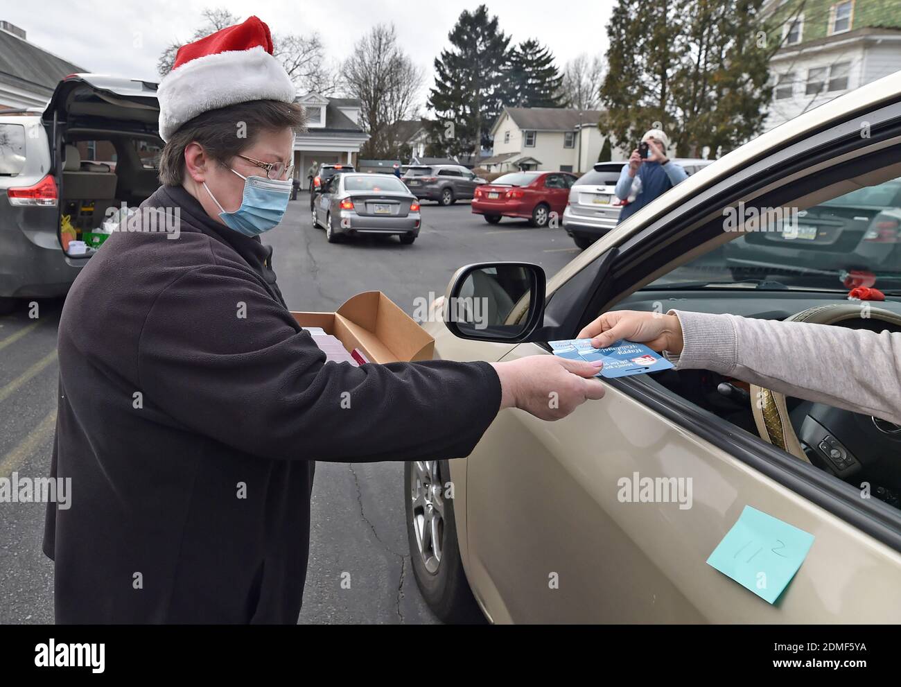 Kingston, United States. 16th Dec, 2020. A volunteer hands a food pantry guest a gift card for groceries to go along with the food they supply.Since the start of Covid the Al Beech food pantry has been very busy, today they served there one millionth guest. For Christmas volunteers wore Santa hats and handed out gift cards, candy and balloons along with the regular food goods. Credit: SOPA Images Limited/Alamy Live News Stock Photo