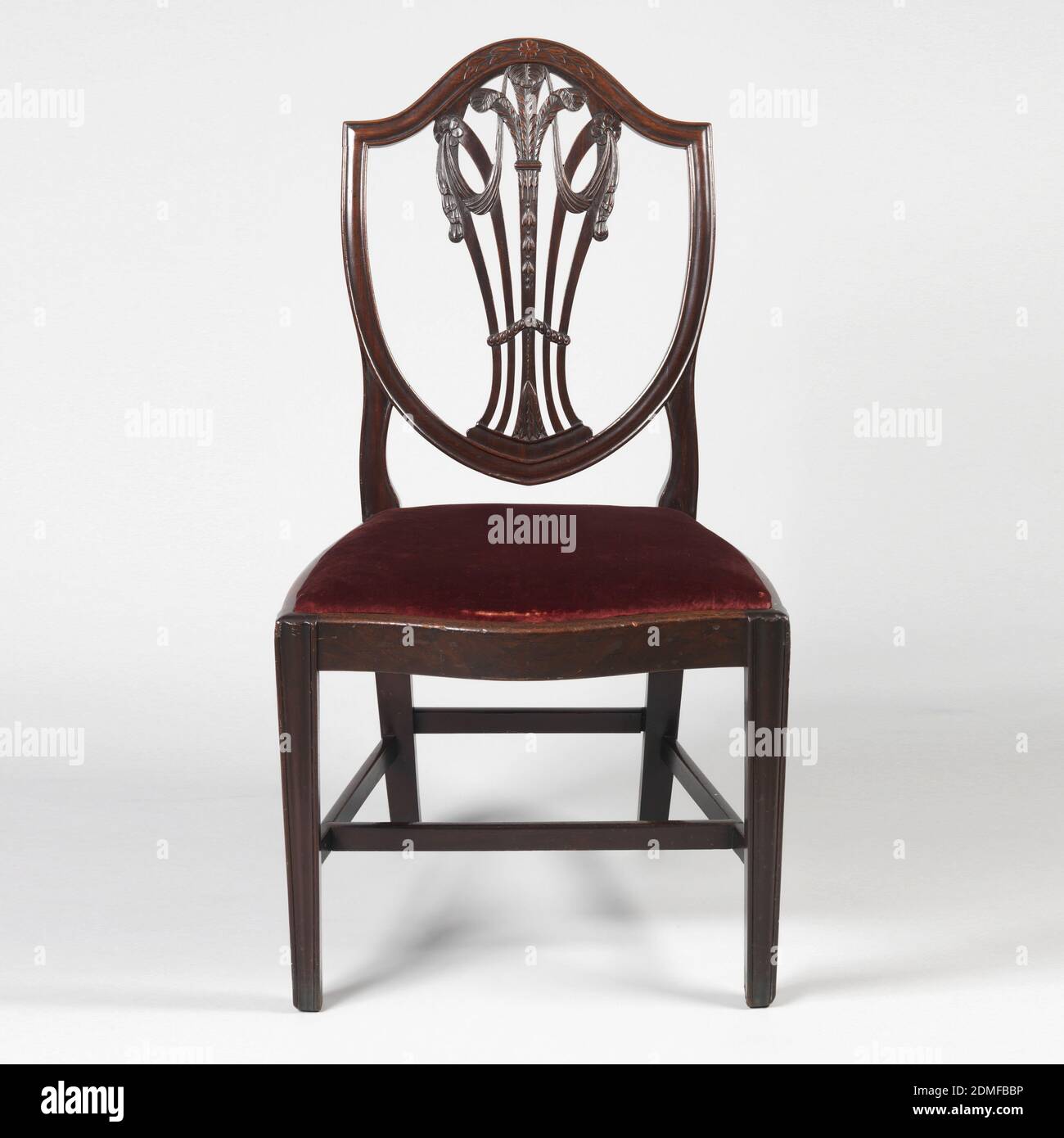 Side chair, Mahogany, Shield-shaped back. The vase shaped openwork vertical splat consists of five curved vertical slats-- the center one is carved with foliage at the base; the branches into three ostrich feathers. Splats on both sides curving outwards meet those on the outside in two rosettes, from which swags of drapery hang. The front legs are moulded and slightly tapered. Front seat rail is serpentine and side rails are bowed slightly. There is a drop in seat covered in silk solid cut stamped cloth velvet., England, ca. 1780, furniture, Decorative Arts, Side chair Stock Photo