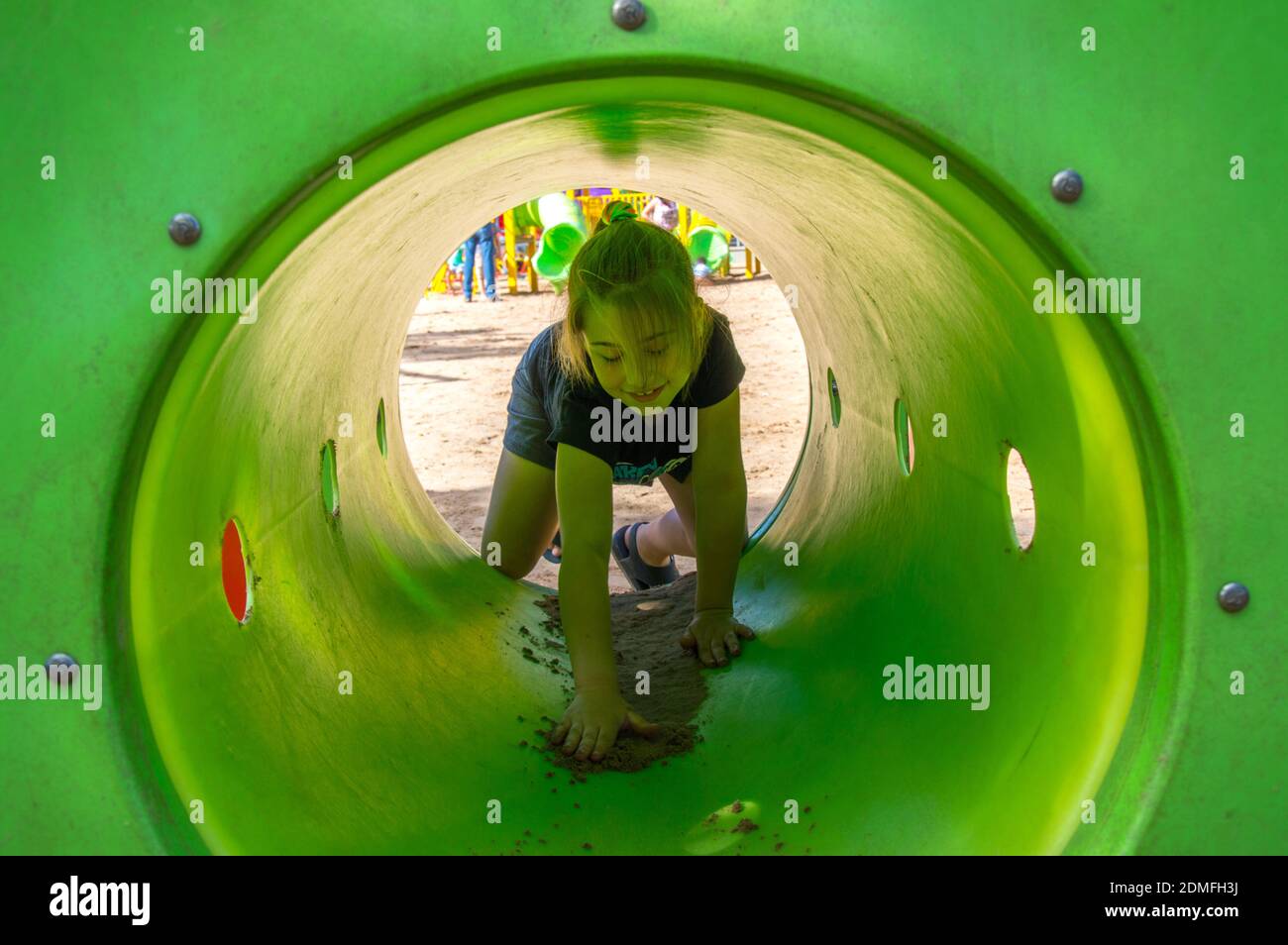 Girl Playing In Green Tube At Playground Stock Photo