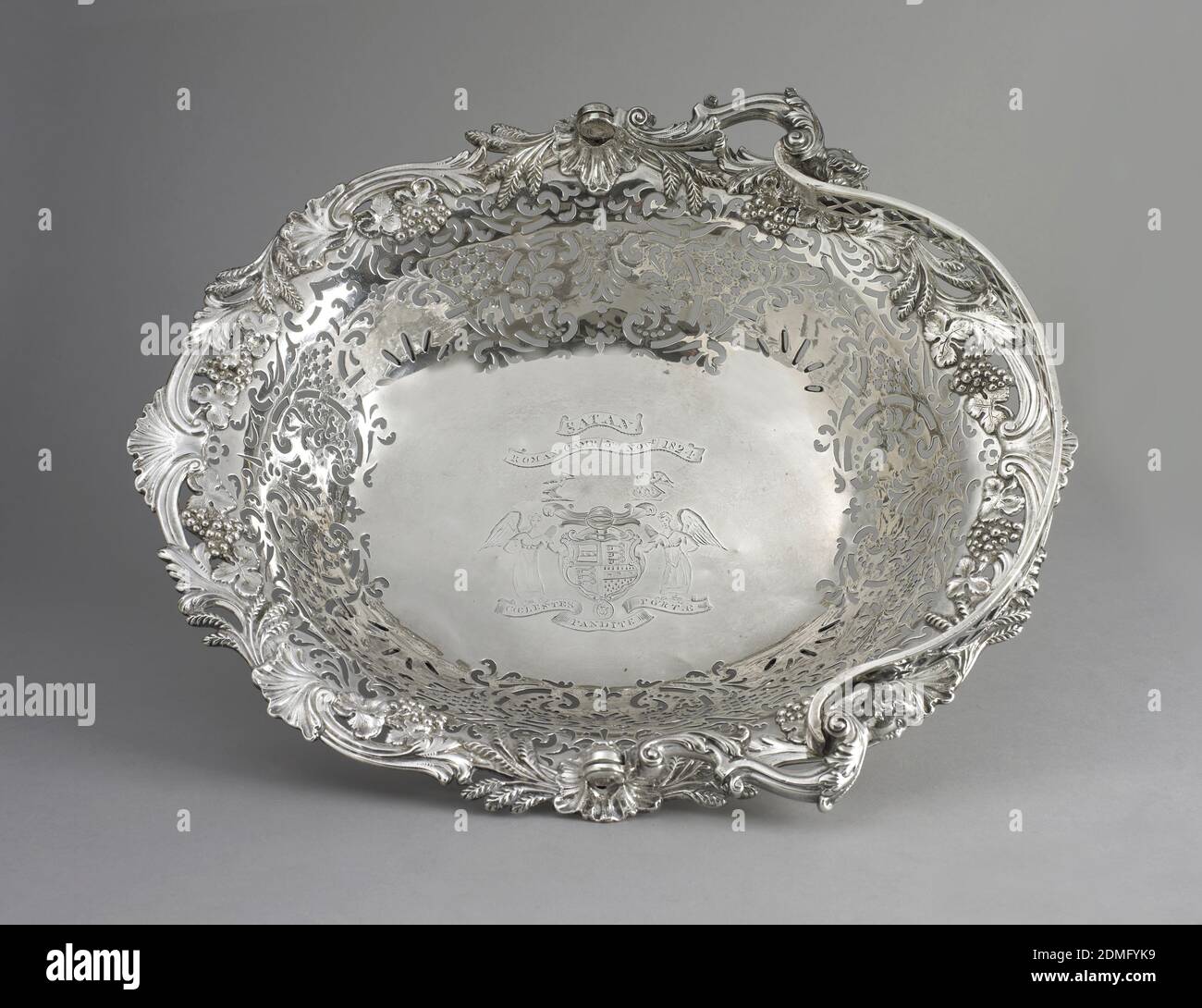 basket, silver, George II cake basket. Oval basket ajoure with rosetted trelliswork and foliate devices, the rim applied with grape clusters and wheat ears; the hinged bail handle with enleafed scrolls and female busts; on scroll feet headed with a frilled shell., London, England, 1758, metalwork, Decorative Arts, basket Stock Photo