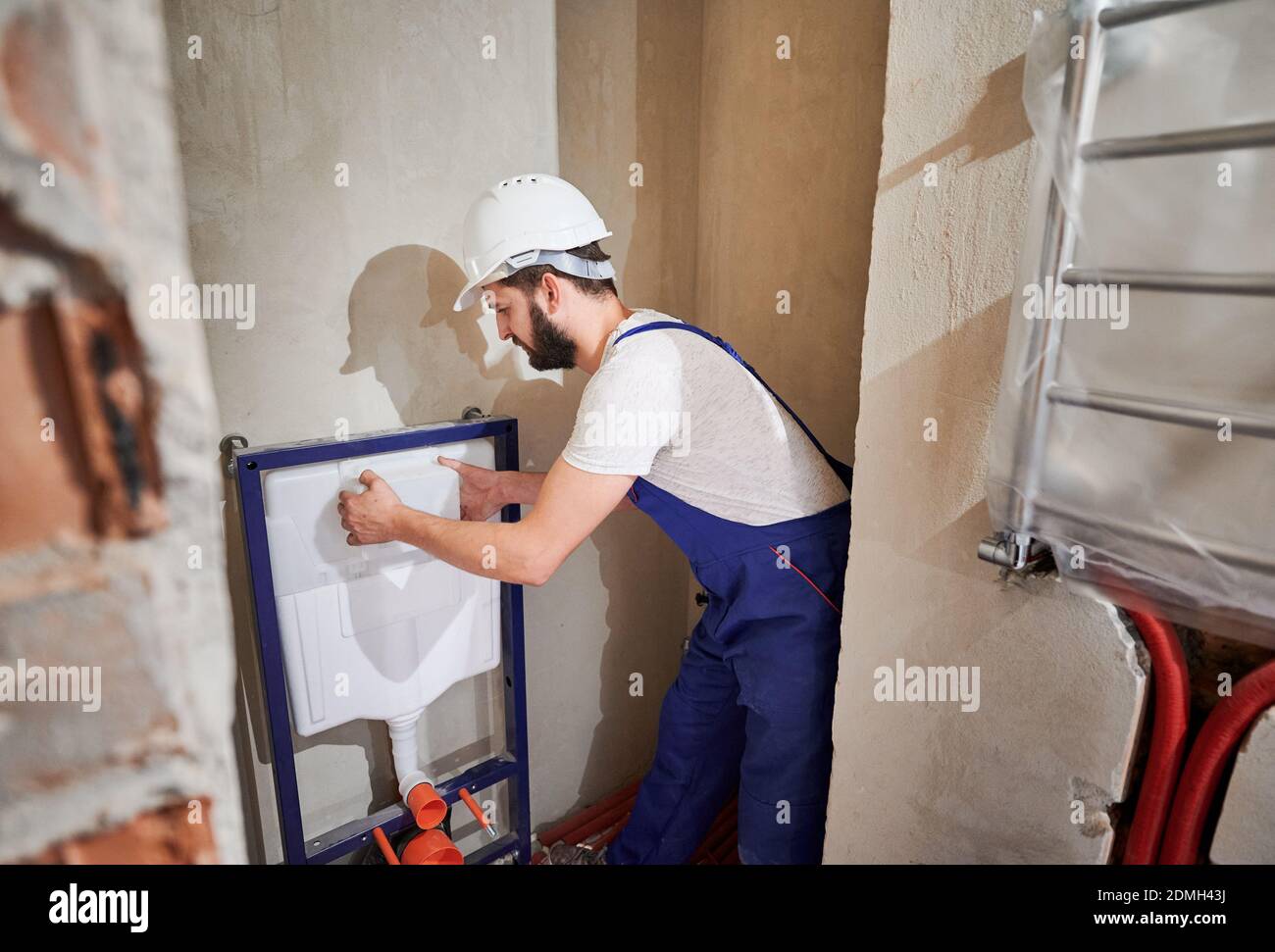 Male plumber in work overalls installing concealed toilet frame in