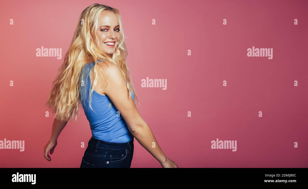 Side view portrait of smiling woman standing on pink background. Cheerful woman with a beautiful smile. Stock Photo