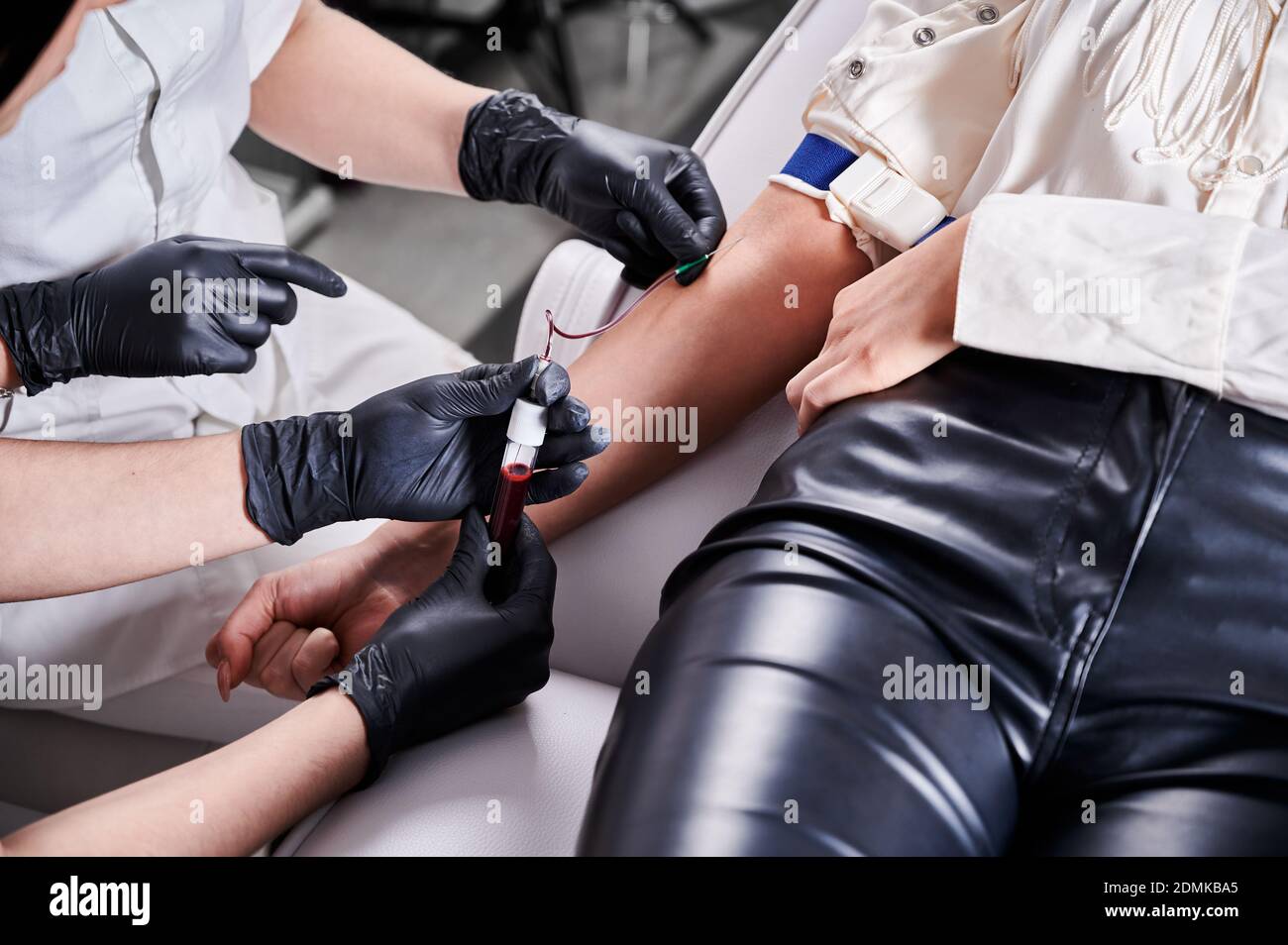 Process of taking blood sample in blood tube from a patient in a chair in beauty salon. Young brunette girl sitting in chair before platelet-rich plasma therapy. Concept of skincare treatment. Stock Photo