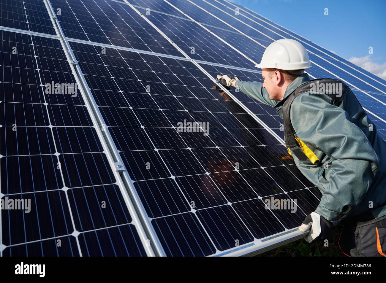 Man technician in safety helmet repairing photovoltaic solar module. Electrician in gloves maintaining solar photovoltaic panel system. Concept of alternative energy and power sustainable resources. Stock Photo