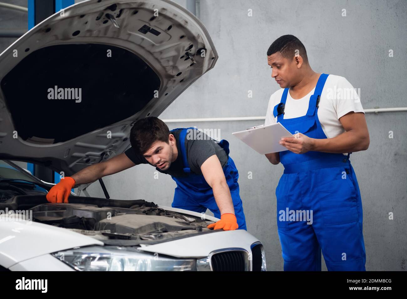 Two mechanics inspect the engine of a car and discuss repair Stock