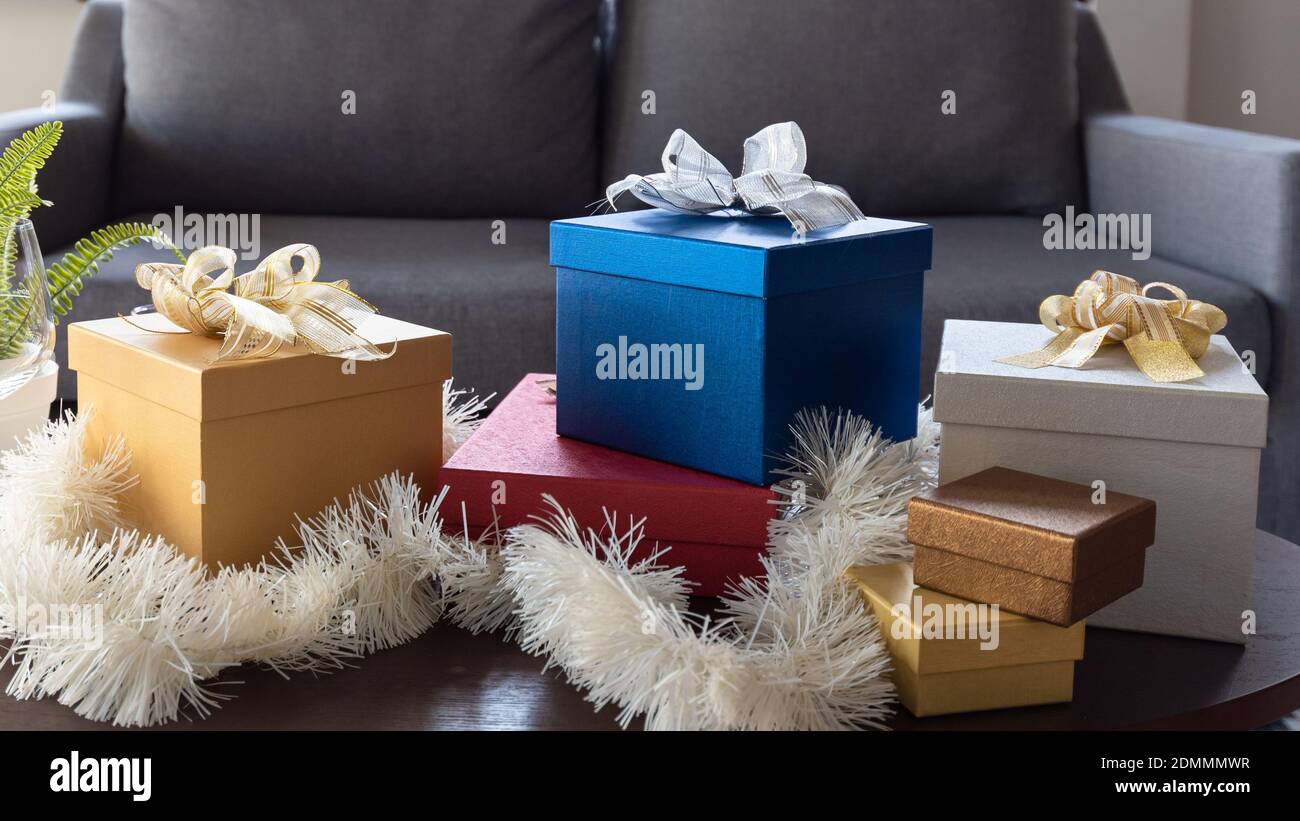 Beautiful Christmas gift boxes wrapped in colourful paper with ribbon bow on table in living room at home Stock Photo