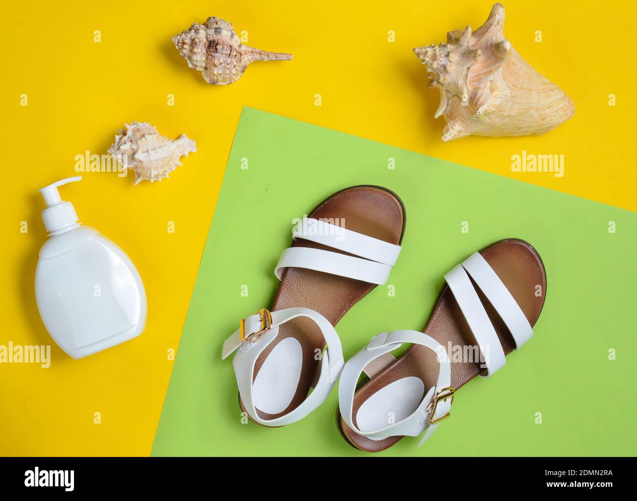 Fashionable leather women's sandals, seashells, sunblock on colored pastel background, top view, flat lay Stock Photo