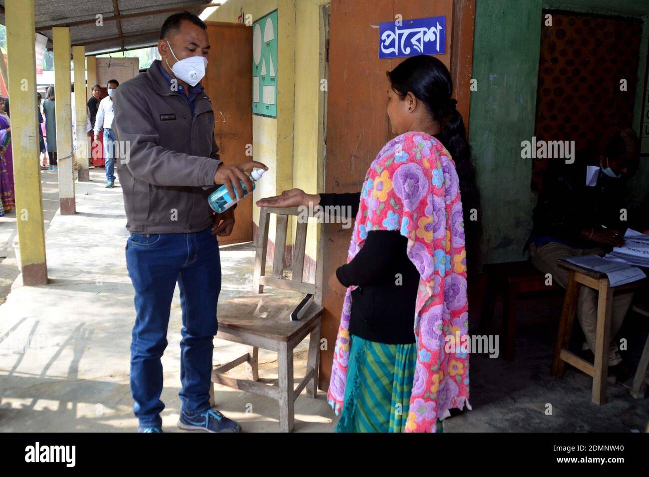 Nagaon, Assam, India - 17  December 2020: A  health worker spraying hand sanitizer to all voters standing in queue due to Covid - 19 pandemic at a Polling station during the Tiwa Autonomous Council election in Kachamari village in Nagaon district of Assam, India.        Credit: DIGANTA TALUKDAR/Alamy Live News Stock Photo