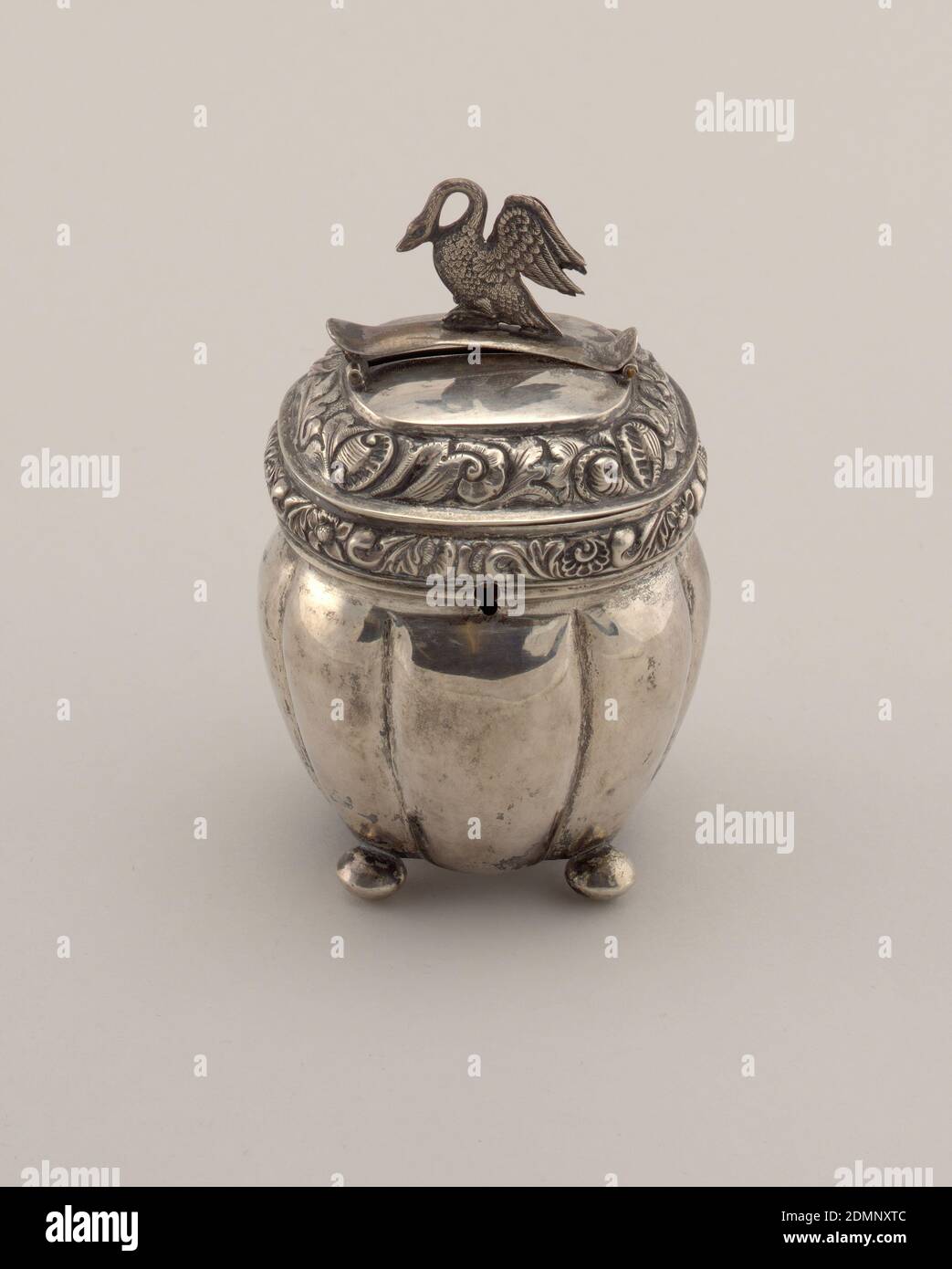 Coin bank, Silver, Coin bank with lobed body on ball feet. Lid with floral repousse work and chasing. Hinged finial with a cast swan. Keyhole at front center., Probably Netherlands, 19th century, metalwork, Decorative Arts, Coin bank Stock Photo