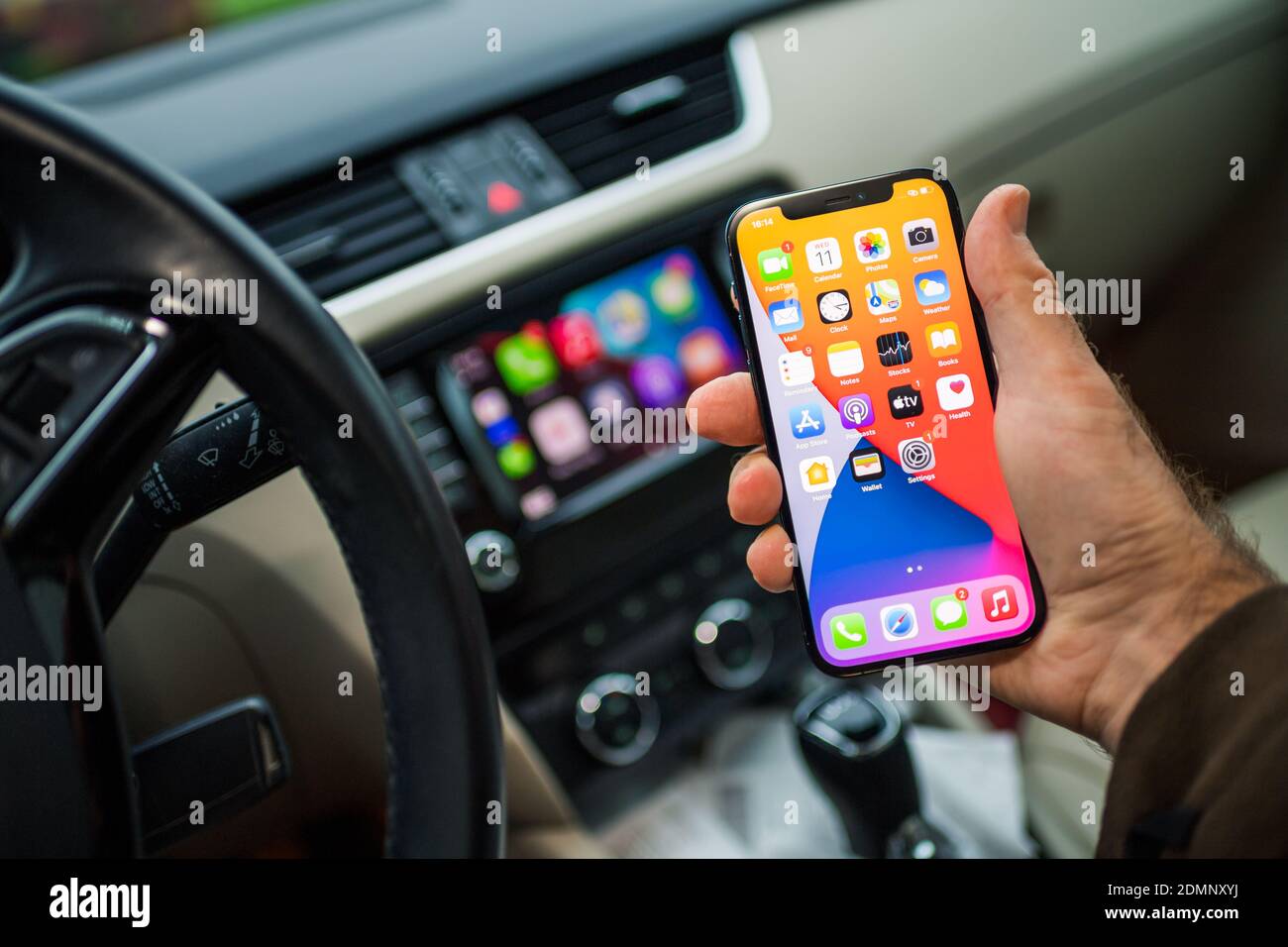 Paris, France - Nov 11, 2020: POV male driver holding new iPhone 12 Pro smartphone with infotainment car computer system running Apple Computers CarPlay from iOS in background Stock Photo