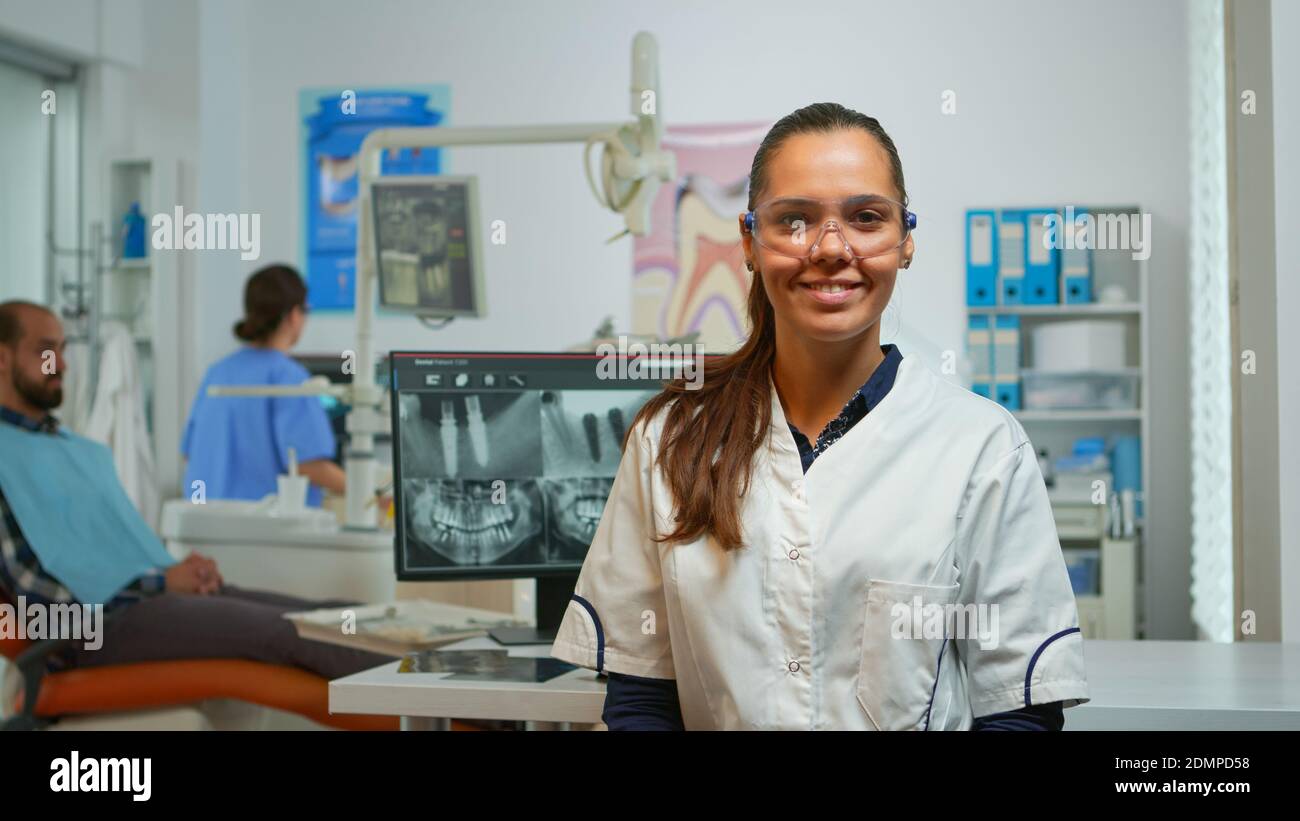 Stomatologist doctor smiling at camera in dental office while assistant