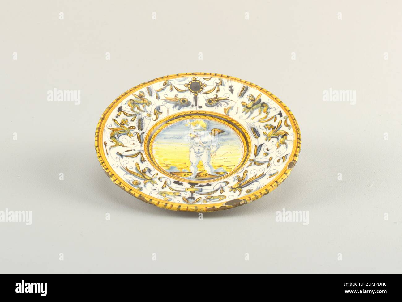 Amorino, Tin-glazed earthenware (maiolica), Plate with image of blindfolded Cupid at center. Rim decorated with grotesques. Yellow dash border., possibly Urbino, Italy, possibly ca. 1600, ceramics, Decorative Arts, Plate, Plate Stock Photo