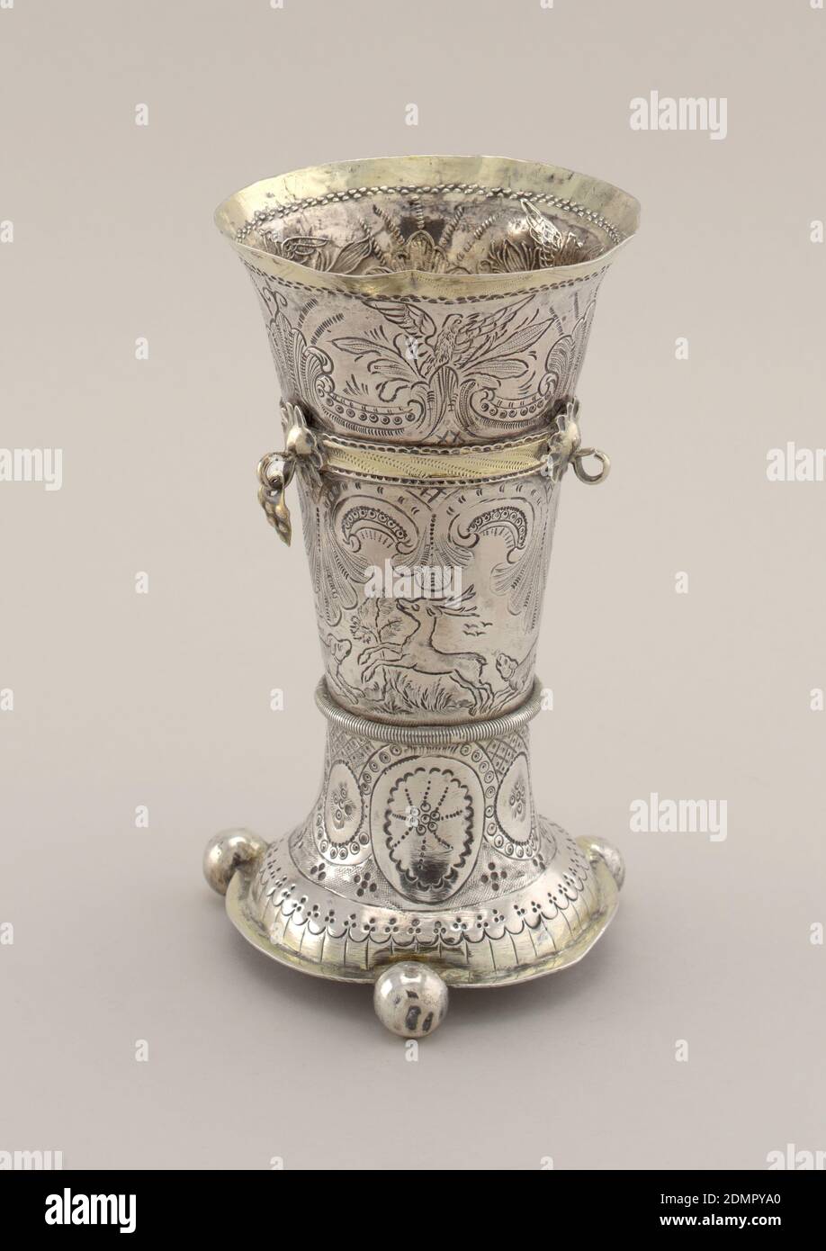 Beaker, Chased and parcel-gilt silver, Spreading domed foot on three balls. Flaring body in three sections with three rings attached to upper band, two of them with lozenge-shaped pendants (third missing). Lower section engraved with oval ornaments; middle section, engraved with hunting scene, the upper with three spread eagles and scrolls. Rim, foot and bands gilt., Bergen, Norway, 1767, metalwork, Decorative Arts, Beaker Stock Photo