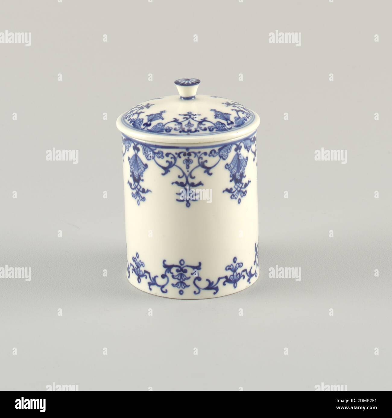 Pomade Jar (Pot à Pommade or Pot à Fard), Saint-Cloud Porcelain Manufactory, French, active by 1693 - 1766, soft paste porcelain, vitreous enamel, Cylindrical form featuring arabesque or lambrequin motifs wrapped around entire circumference of pot on both upper and lower edges, all in underglaze blue; similar motif wrapped around edge of lid; knob on top of lid features single fower motif; all on white ground., France, ca. 1730, ceramics, Decorative Arts, jar, jar Stock Photo