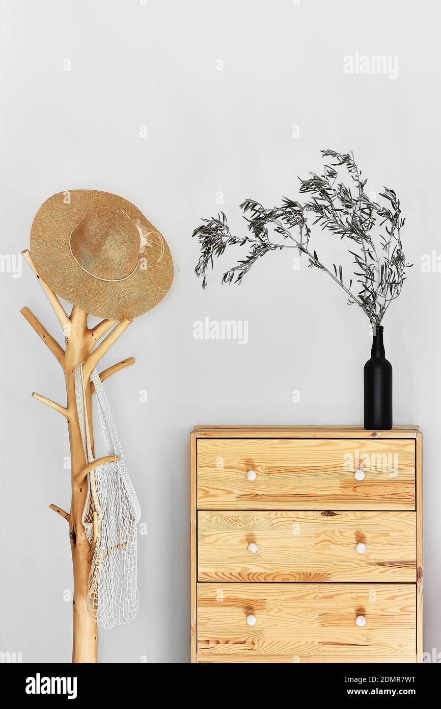Minimalistic hallway interior with trendy wooden clothes hanger stand and commode against a gray wall. Wicker hat and bag on the hanger. Copy space. Stock Photo