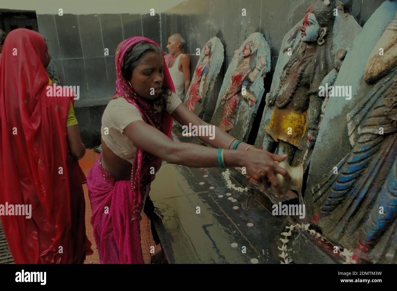 A pilgrim pouring water after praying in front of Hindu deities, a ...