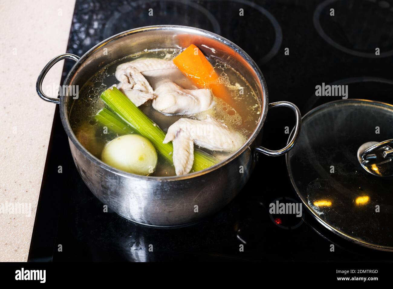 above view of chicken wings broth is boiled in steel stewpot on stove at home kitchen isolated on white background Stock Photo