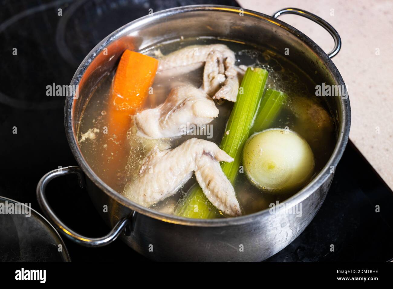 chicken wings soup is cooked in steel stewpot close up on stove at home kitchen isolated on white background Stock Photo
