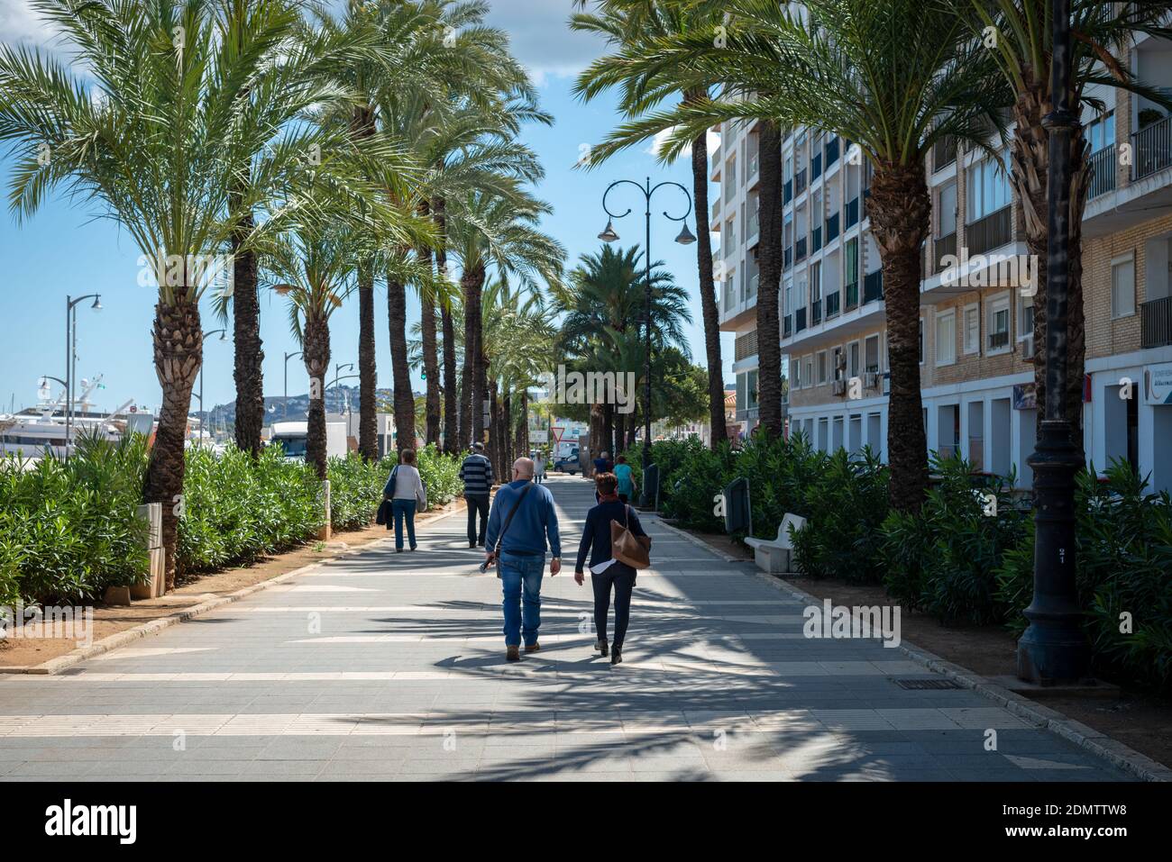 Denia, Costa Blanca, Alicante, Spain.People walk along a footpath lined by palm trees in the Mediterranean coastal town. Stock Photo