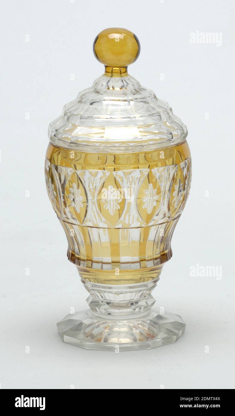 Jar and lid, Glass, Ogee-shaped body on short stem with faceted knop and 12-sided flaring foot; sides cut to reveal clear glass behind flashed amber layer in pattern of rosettes in oval frames and underneath alternate colored vertical stripes; domed, stepped cover, faceted, with amber ball finial., Europe, 19th century, glasswares, Decorative Arts, Jar and lid Stock Photo