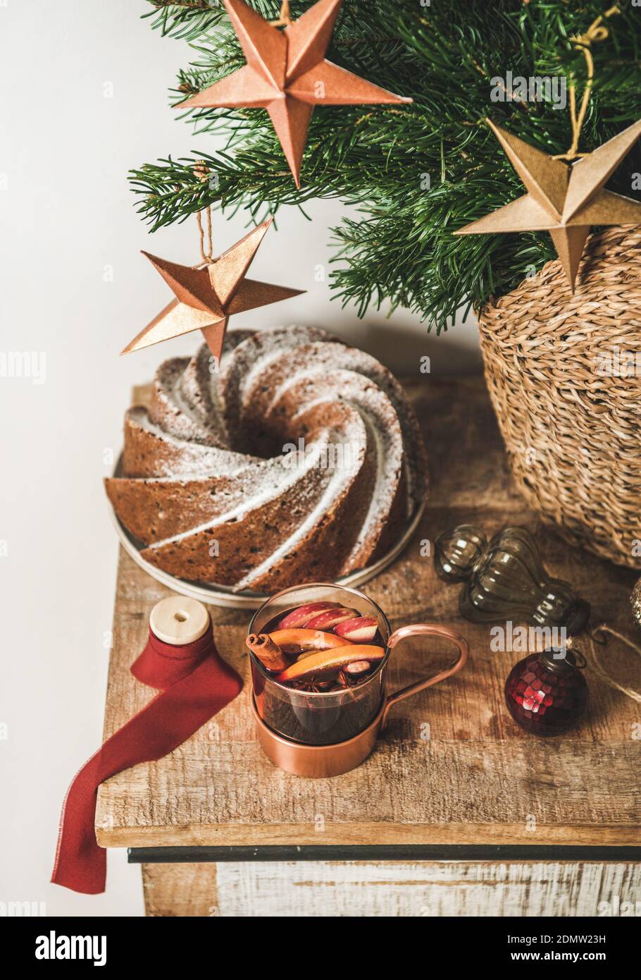 Cup of mulled wine and Christmas bundt cake over wooden kitchen counter with festive decorative baubles and stars and Christmas tree branches at background. Winter holiday mood concept Stock Photo