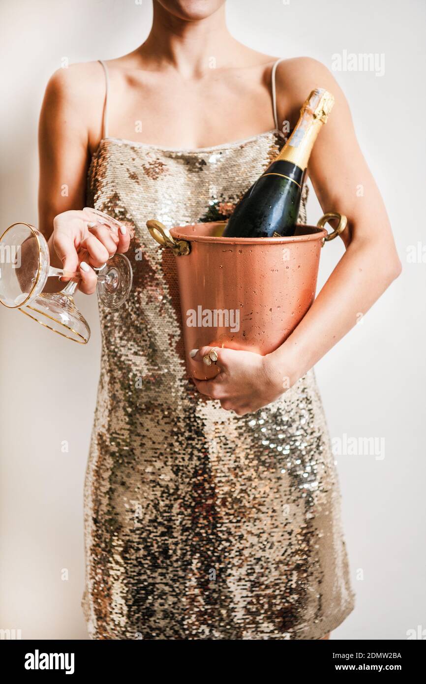 Young woman figure in festive glittering cocktail golden mini dress holding copper bucket for champagne and glasses over white wall background. New Year holiday party concept Stock Photo