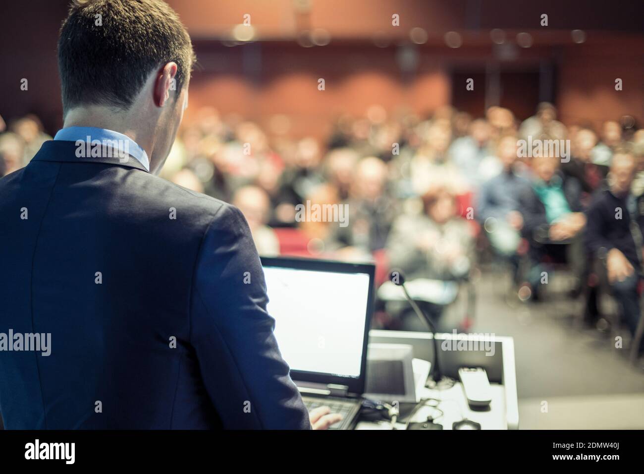 Speaker giving a talk in conference hall at business meeting event. Rear view of unrecognizable people in audience at the conference hall. Stock Photo