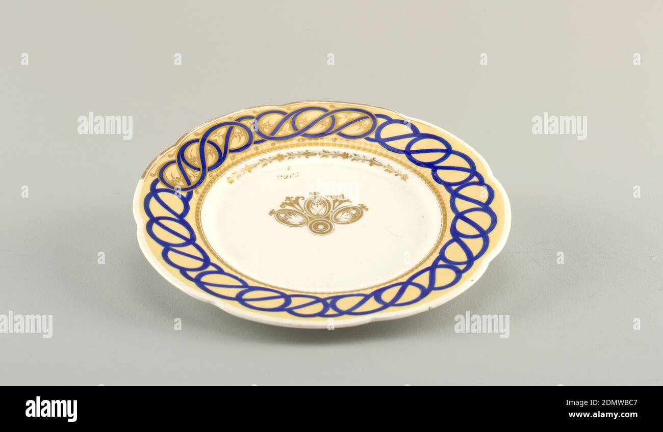 Sample Plate, hard paste porcelain, vitreous enamel, gold, Circular plate, the white body showing progressive sections of decoration around the scalloped rim: a tan ground with applied interlaced curving blue bands, and gilt floral border; the well with a section of gilt, stylized floral decoration in the center; the gilt numbers '6' over '2605' written above the decoration., England, 1870–1890, ceramics, Decorative Arts, plate, plate Stock Photo