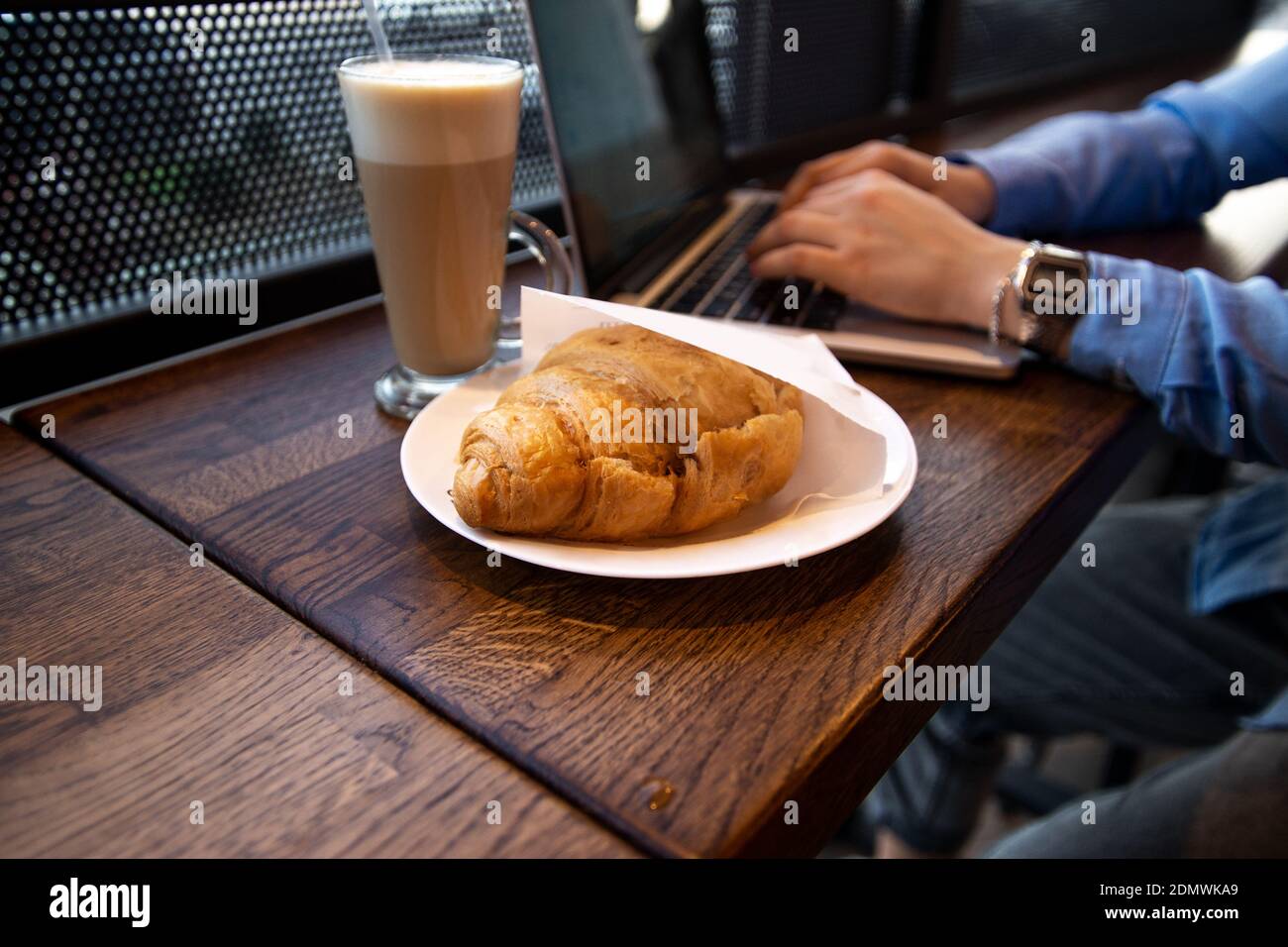 Lunch time concept. Delicate croissant and delicious latte. Close up view of food. Cafe on background. Cozy coffeehouse atmosphere. Female hands typin Stock Photo