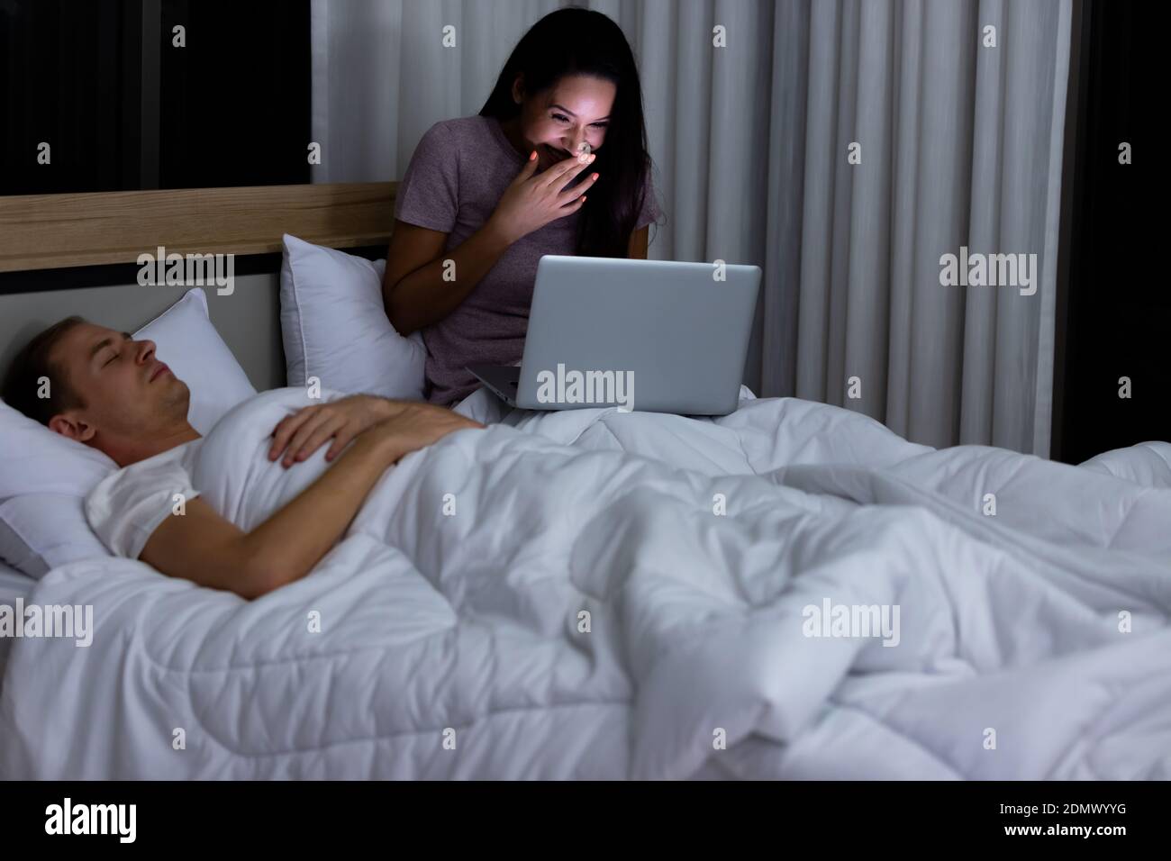 Woman sitting on bed in the night and using laptop computer while
