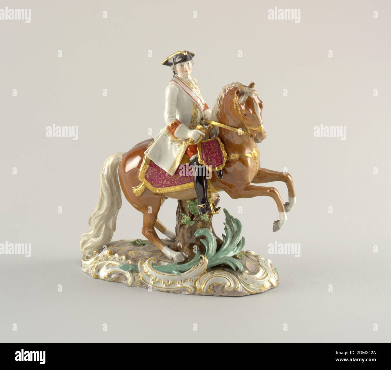 Figure of an Officer on Horseback, Meissen Porcelain Manufactory, German, active from 1710 to the present, hard paste porcelain, vitreous enamel, gold, Officer on horseback. On oval base painted to simulate stone, framed by gilt scrolls. A prancing sorrel supported by tree trunk. An officer on white, gold edged coat and black tricorne in saddle, holding sword hilt in front and reigns in left hand., Germany, mid- 19th century, ceramics, Decorative Arts, figure, figure Stock Photo