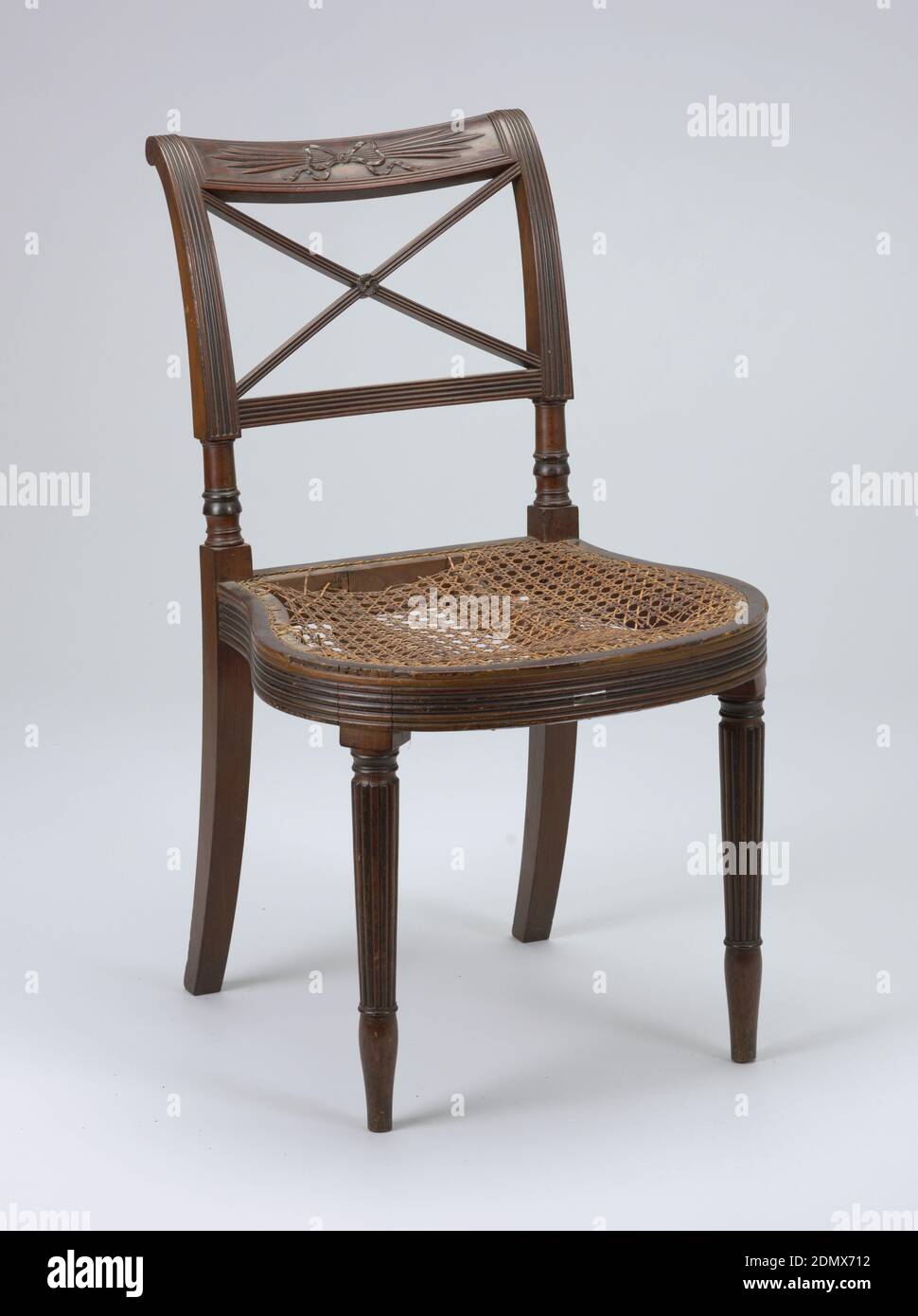 Chair, Mahogany, cane, cotton., Mahogany; caned seat covered with upholstery. Rounded and reeded seat rail; rounded and reeded tapering legs. Top rail carved with 'thunderbolt' design tied with bow. Below top rail, two diagonal, crossing bars, reeded. Set covered with green cotton velvet., New York, USA, ca. 1812, furniture, Decorative Arts, Chair Stock Photo