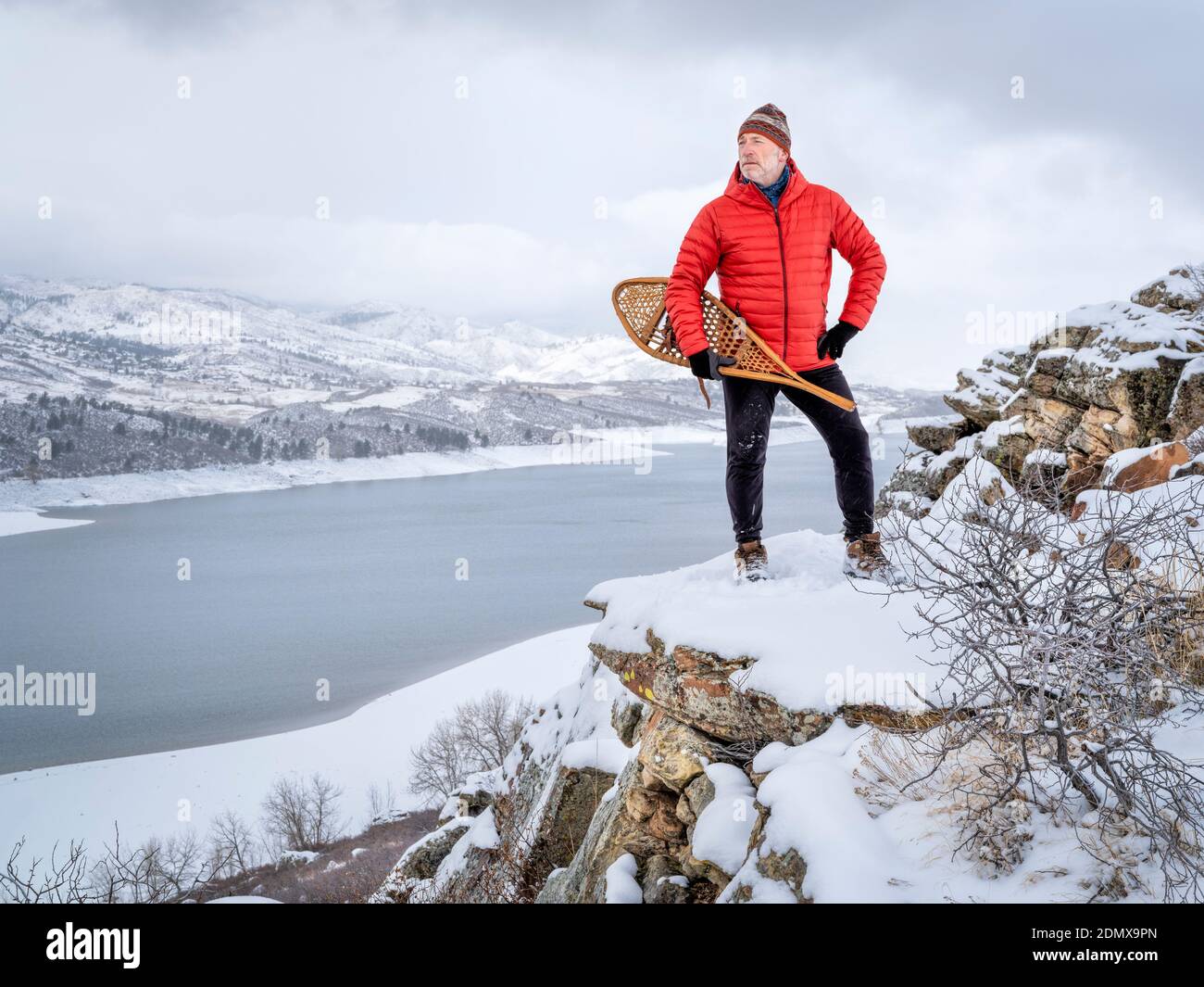 senior man with classic Huron snowshoes is overlooking a mountain lake in winter scenery - Horsetooth Reservoir in northern Colorado Stock Photo