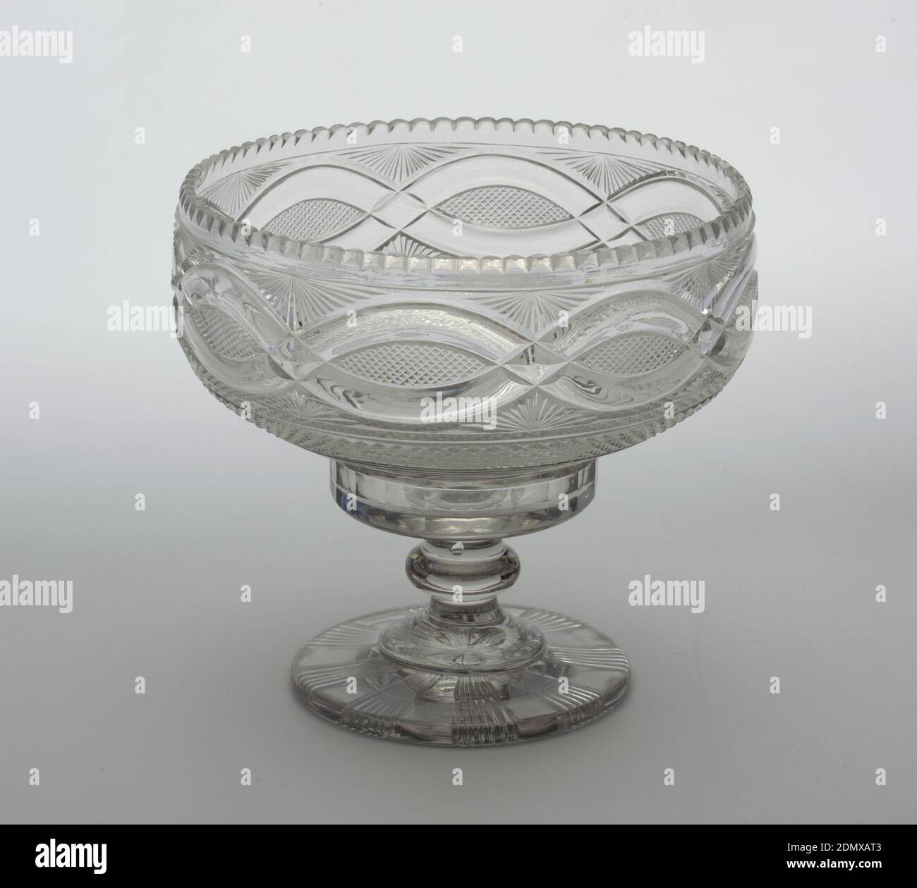Bowl, Glass, Drum-shaped bowl with scalloped edge, the base tapering to a flat bottom, tall stem with central knop, wide flat circular base cut on the bottom with raised flutes; sides of bowl cut with facets at the bottom, bands of prismatic cutting and small diamonds above, a wide band of interlocking loops surrounded by small diamonds and fan cutting., Ireland, ca. 1820, glasswares, Decorative Arts, Bowl Stock Photo