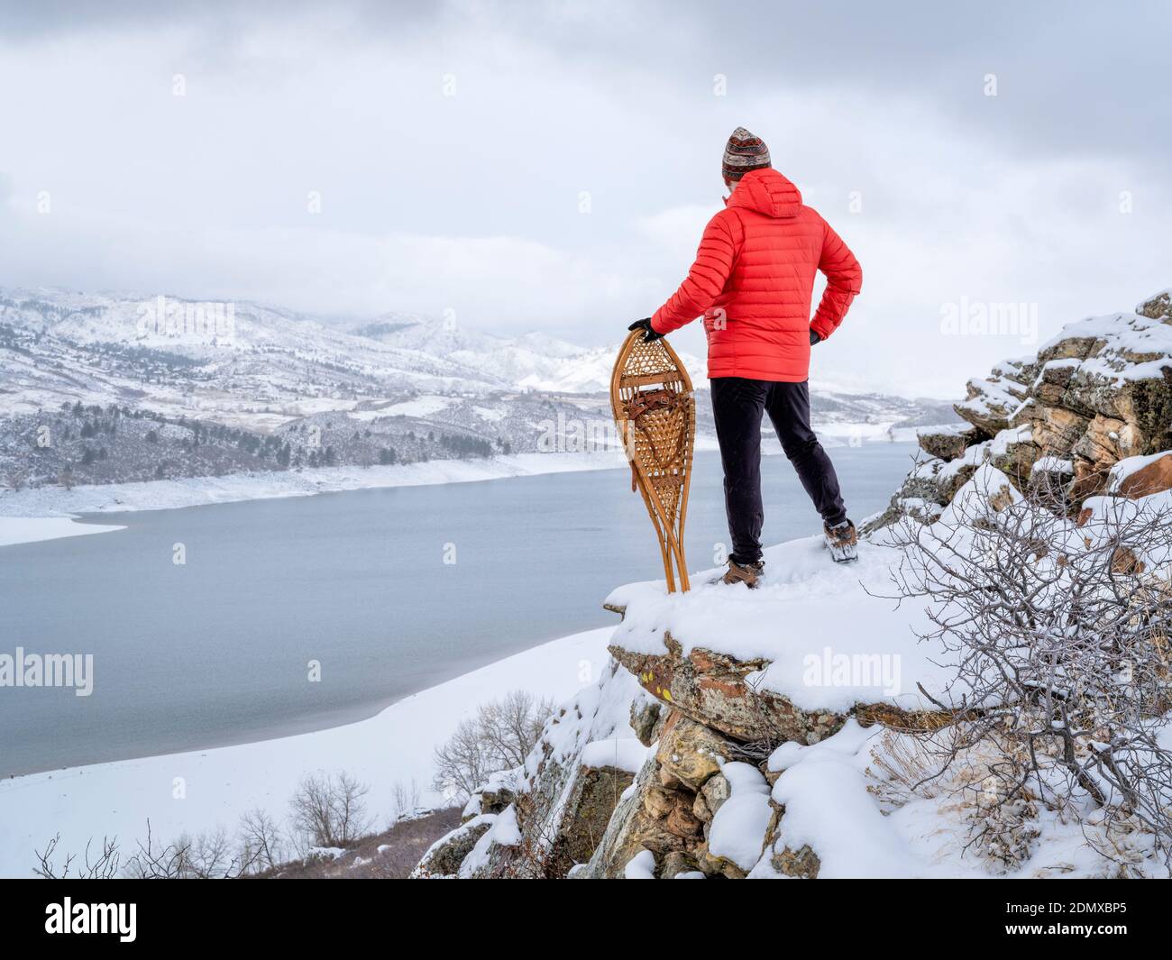 man with classic Huron snowshoes is overlooking a mountain lake in winter scenery - Horsetooth Reservoir in northern Colorado Stock Photo
