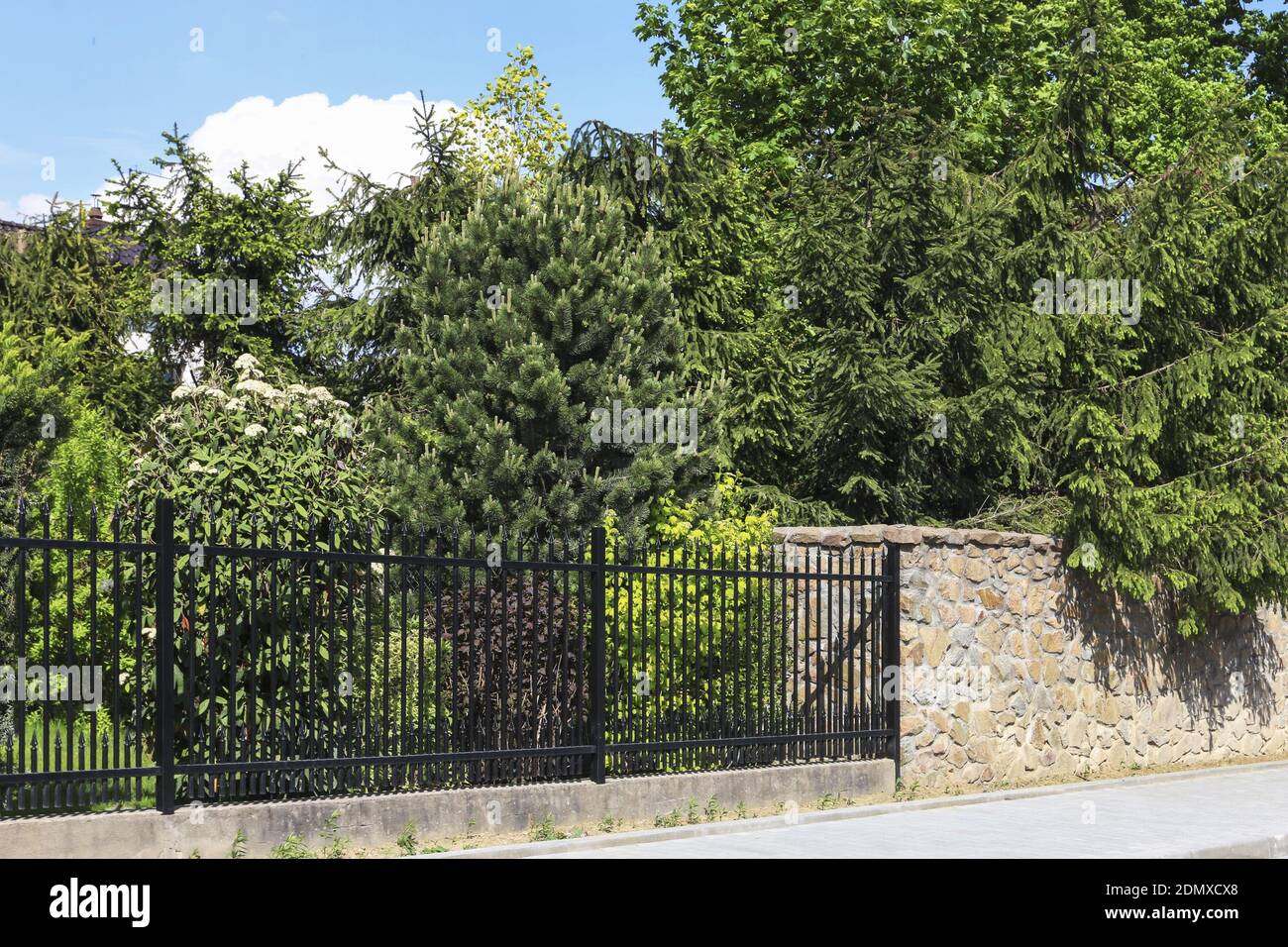 A fence made of stone and other, made of forged elements. Lush garden by the residence. Stock Photo