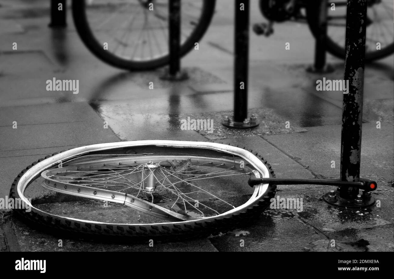 Bicycle buckled front wheel anchored to a rail with a security lock but missing the stolen bicycle. Black and white image with a tiny bit of red. Stock Photo