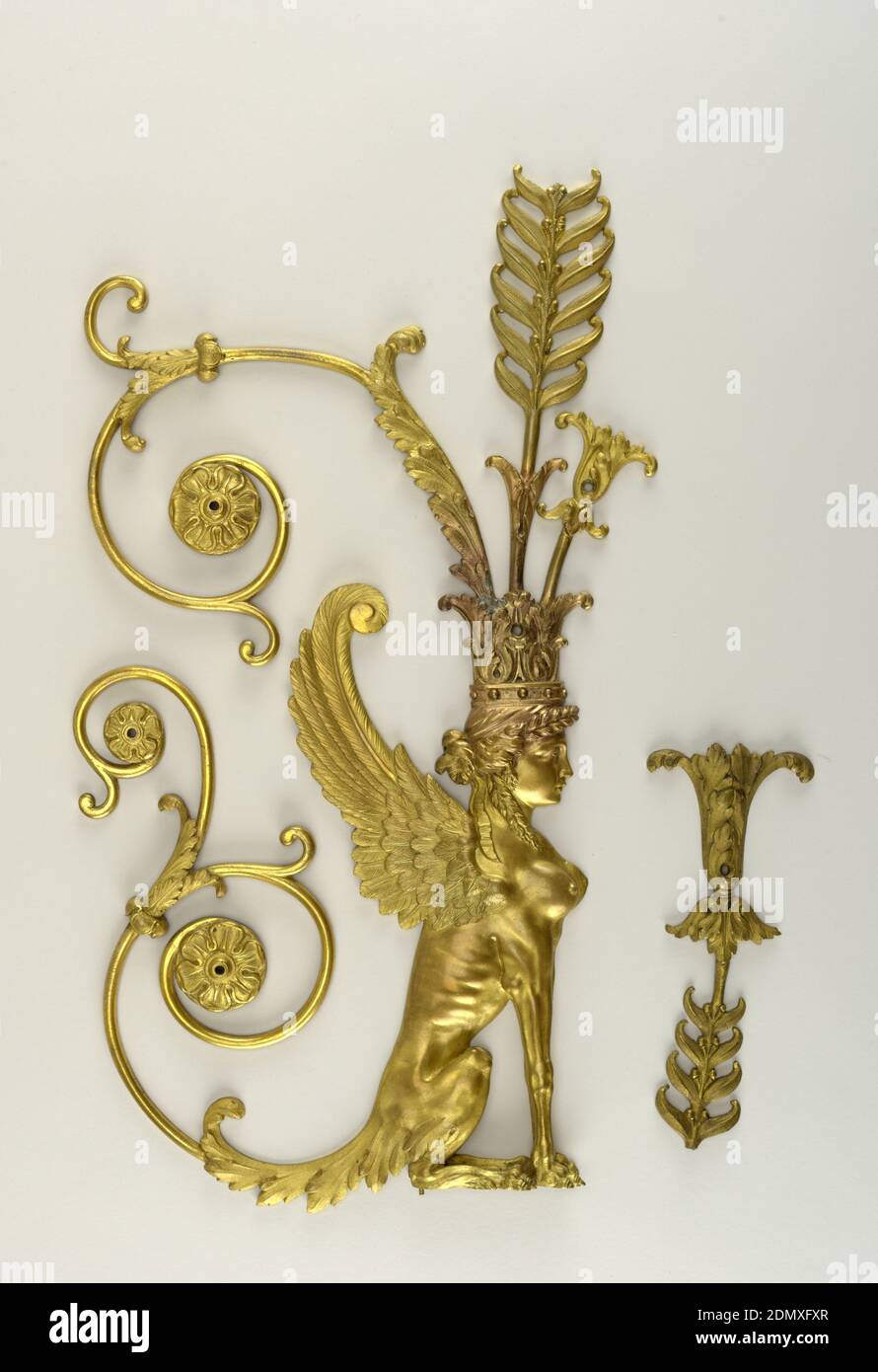 Mount, Gilt bronze, Winged female sphinx facing right with acanthus leaf crown from which springs an ancanthus-like flower, a tall symmetrically leafed and berried stem and a long spiraled leafed stem ending in a rosette. Sphinx's tail is an elongated acanthus leaf ending in a double spiraled stem, each of which terminates in a rosette. Seven screw holes and two small threaded projections under feet for attachment to wood. End broken off center stem projecting from crown., ca. 1805, Decorative Arts, Mount Stock Photo