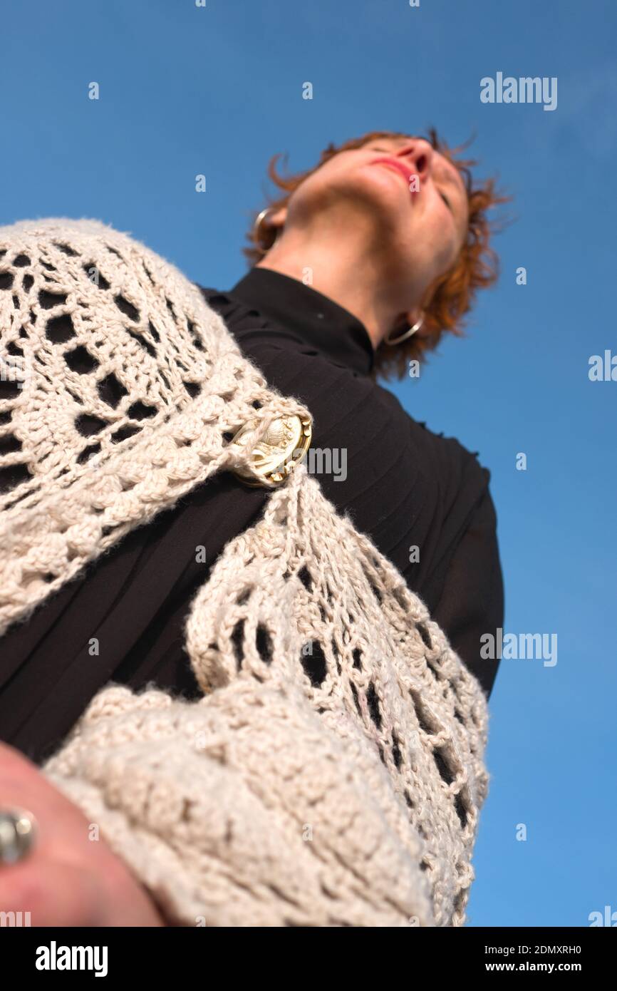 low angle photo of attractive middle aged french woman with a handknitted shawl leaning back as she meditates in the sunlight outside on a clear day Stock Photo