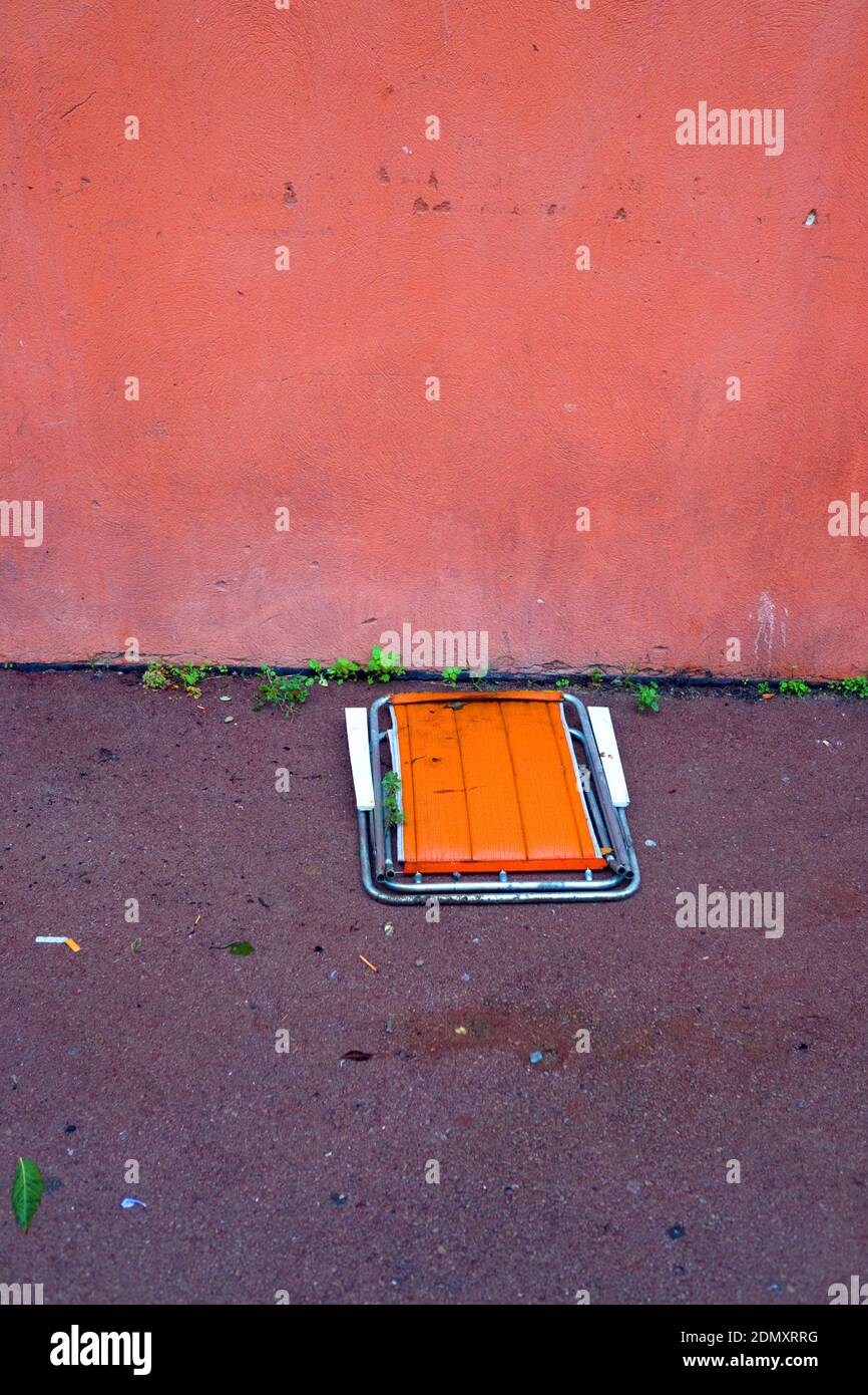 looking down at discarded folded orange deckchair left on pavement in the rain in France Stock Photo